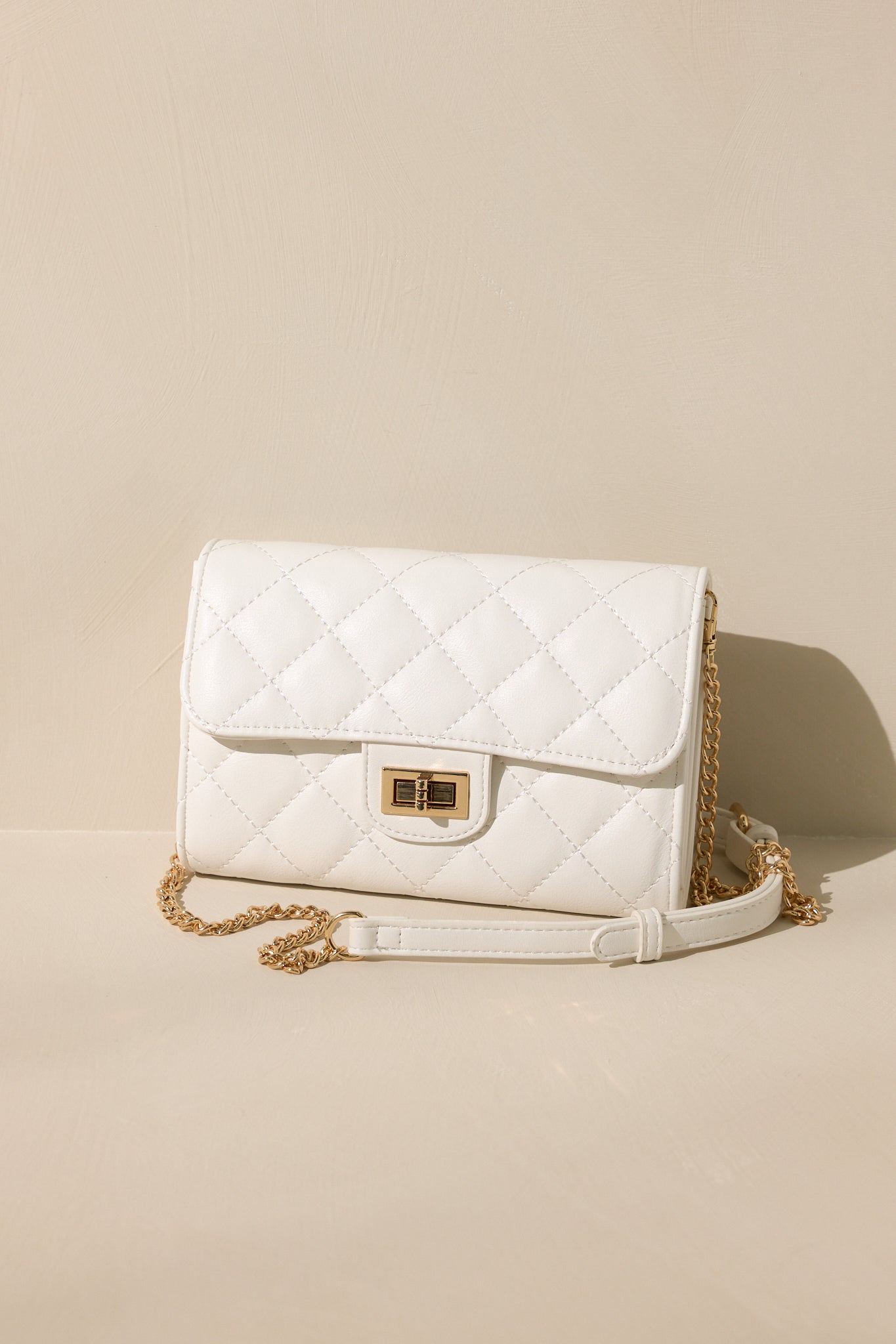 Front view of this white bag that features gold hardware, a quilted design, turn lock closure, a zipper pocket inside, and a detachable chain shoulder strap.