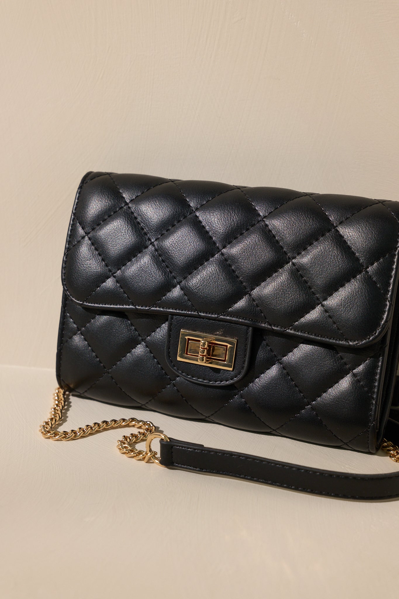 Close-up view of this black bag that features gold hardware, a quilted design, turn lock closure, a zipper pocket inside, and a detachable chain shoulder strap.