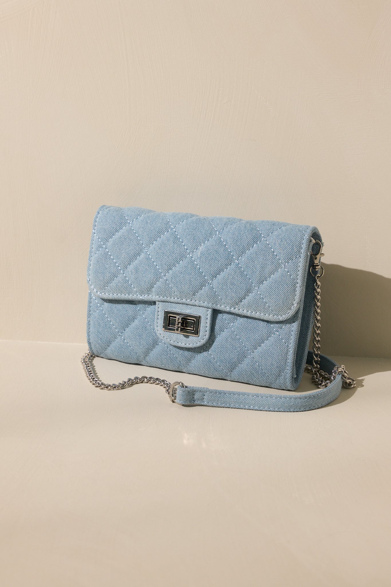 Stand alone view of this denim bag features silver hardware, a quilted design, turn lock closure, a zipper pocket inside, and a detachable chain shoulder strap.