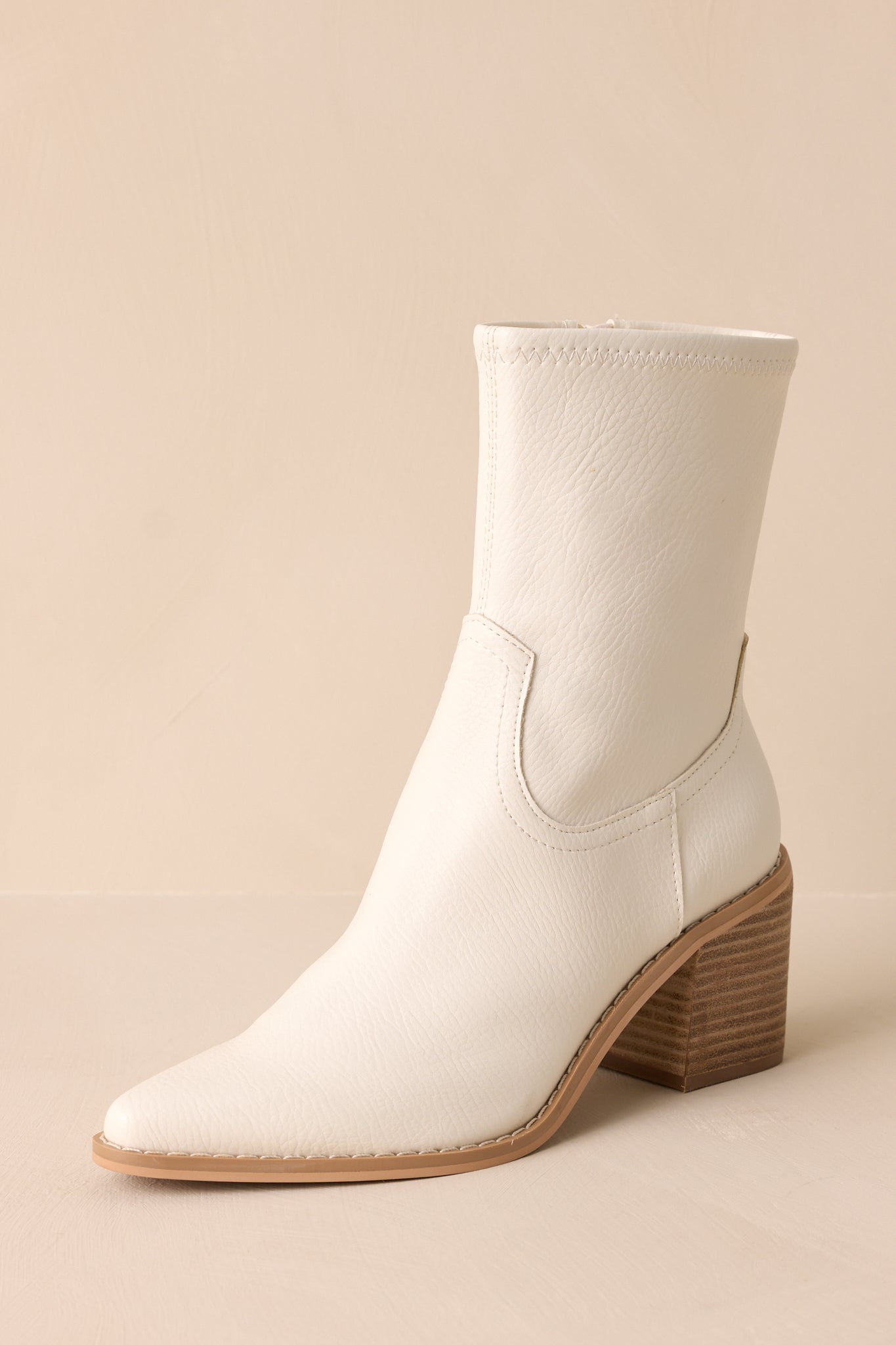 Angled front view of these white boots that feature a pointed toe, a platform heel, a discrete side zipper and a tan sole.