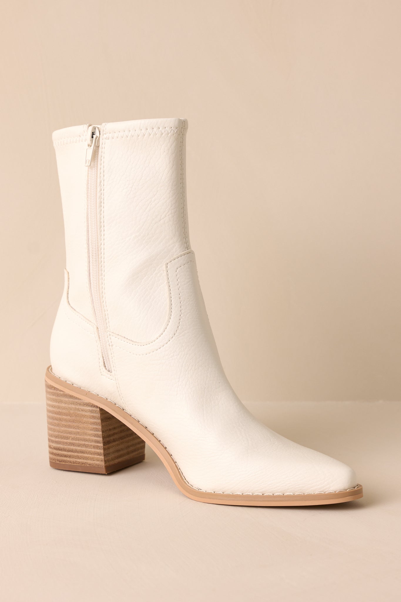 Close-up of the zipper of these white boots that feature a pointed toe, a platform heel, and a tan sole.