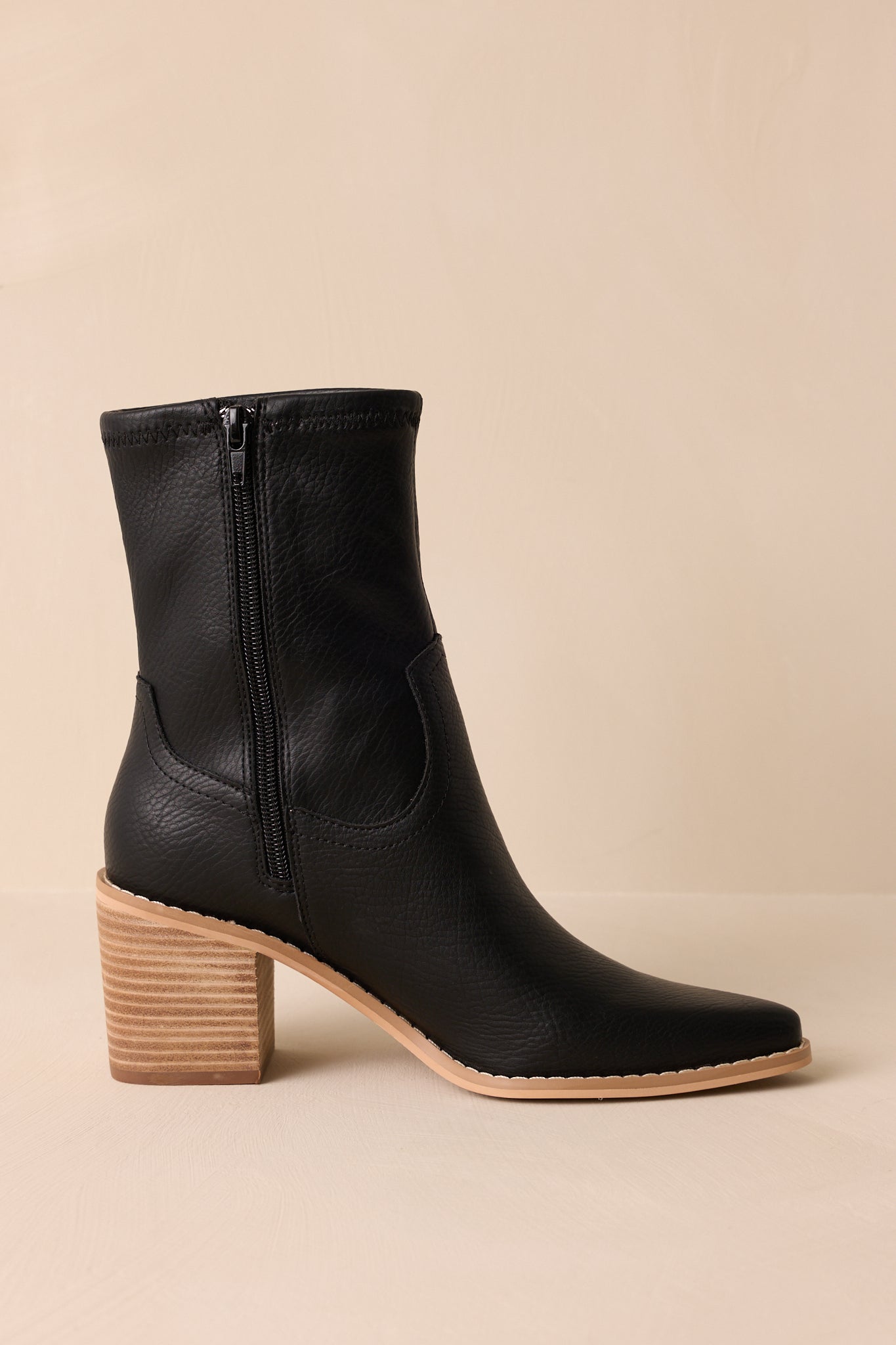 View of these black boots that feature a pointed toe, a platform heel, a discrete side zipper and a tan sole.