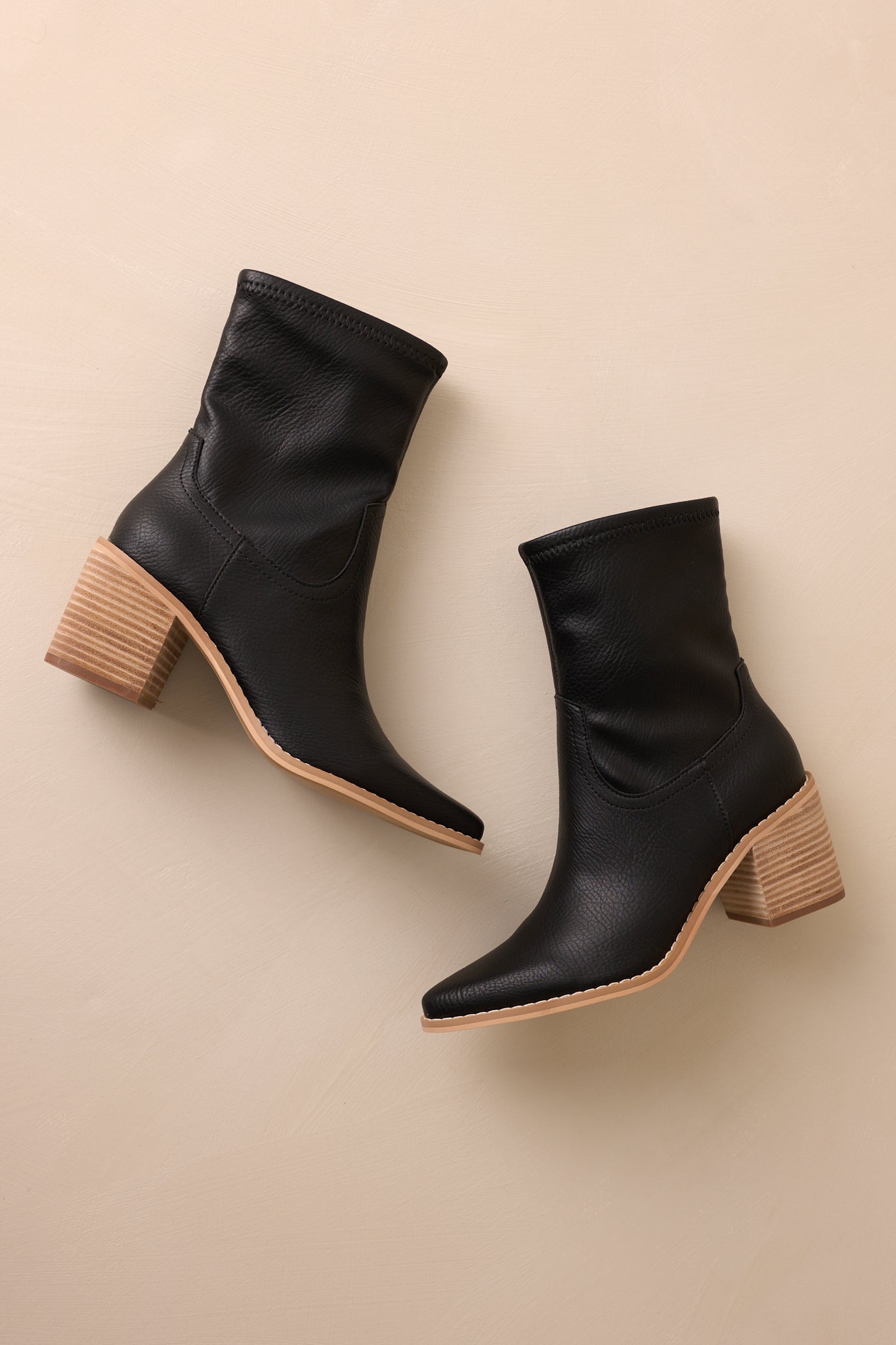 Overhead view of these black boots that feature a pointed toe, a platform heel, a discrete side zipper and a tan sole.