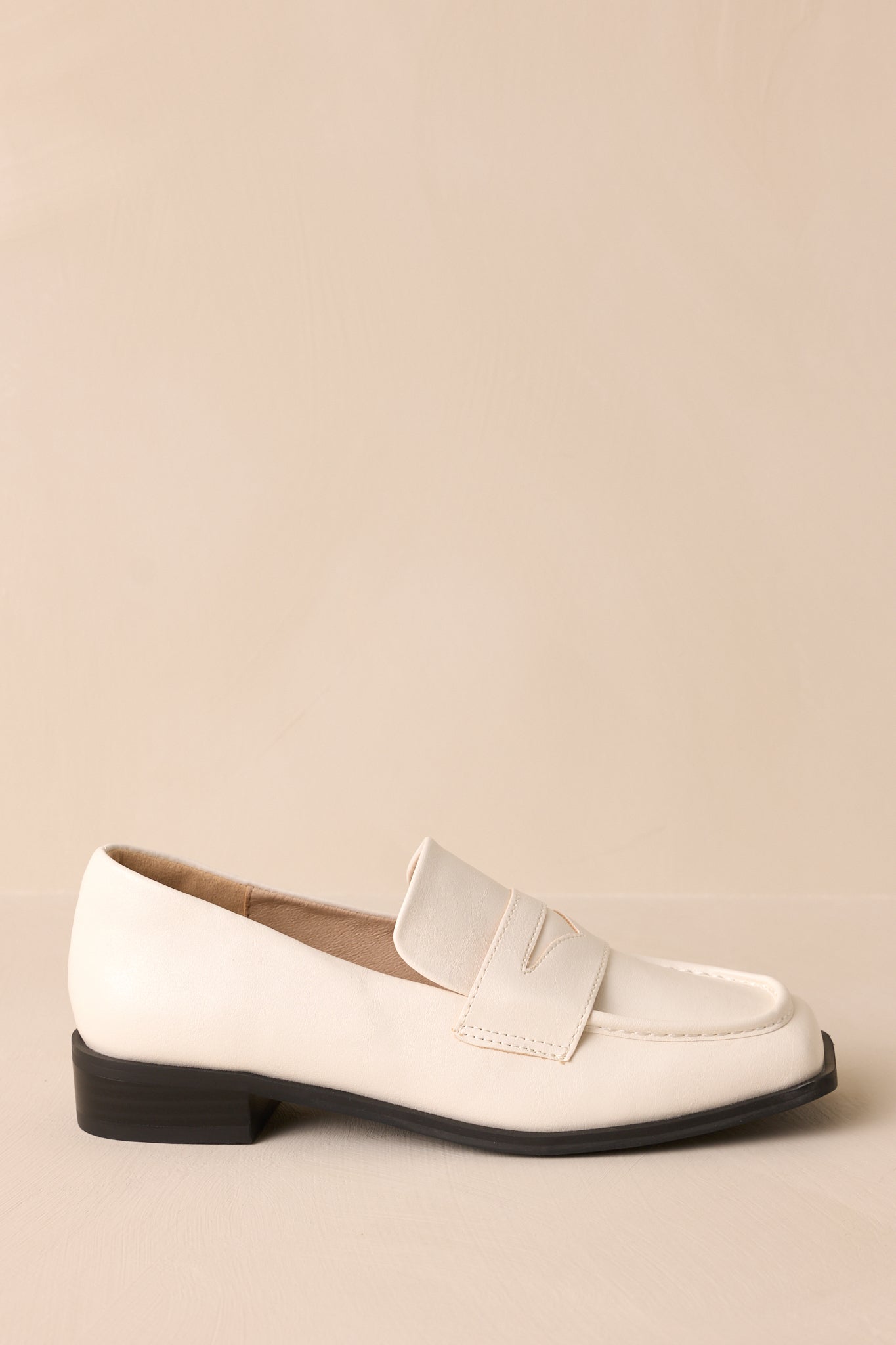 Side view of these white loafers that feature a slip on design, a small heel, a square toe, and a strap across the foot.