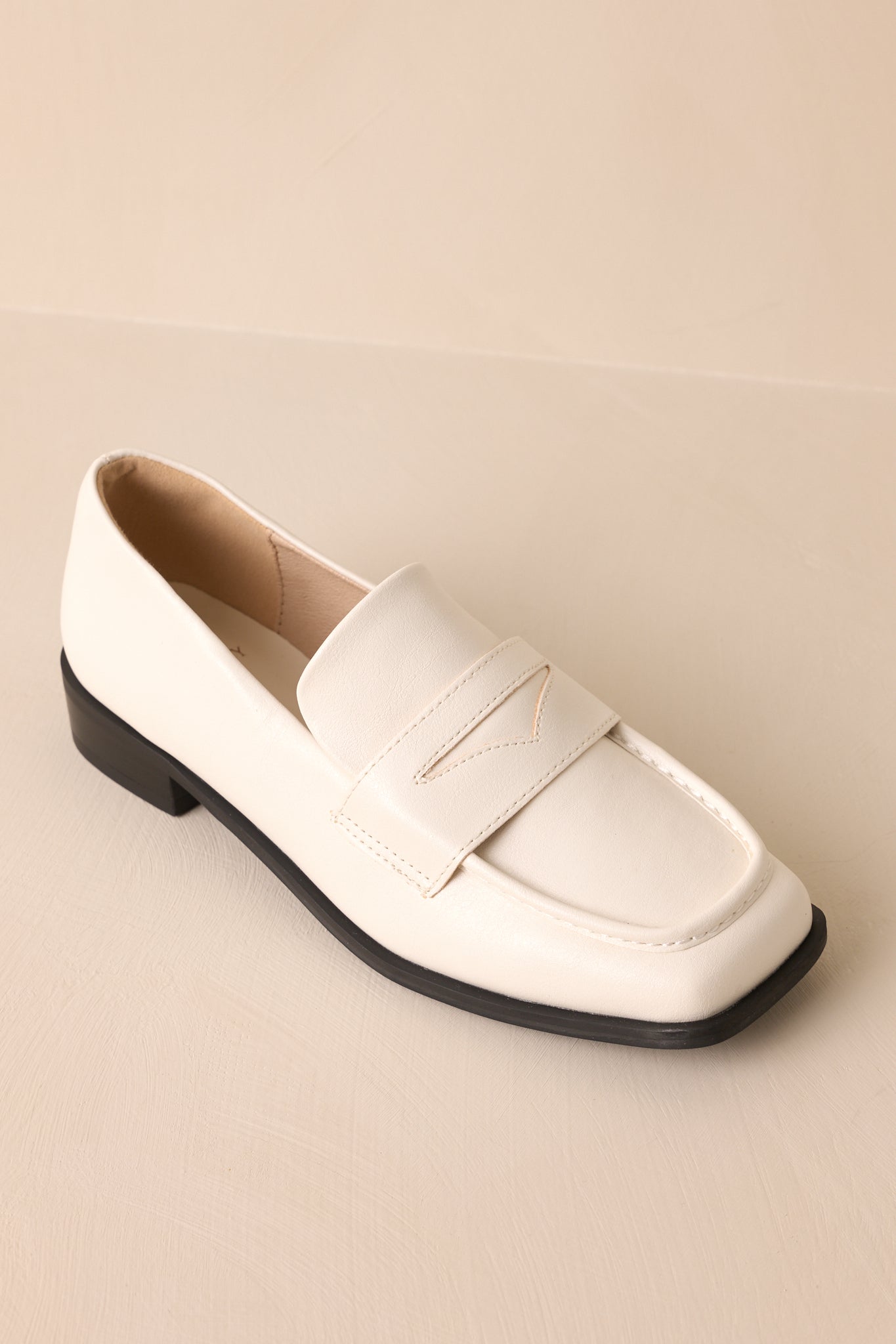 Angled overhead view of these white loafers that feature a slip on design, a small heel, a square toe, and a strap across the foot.