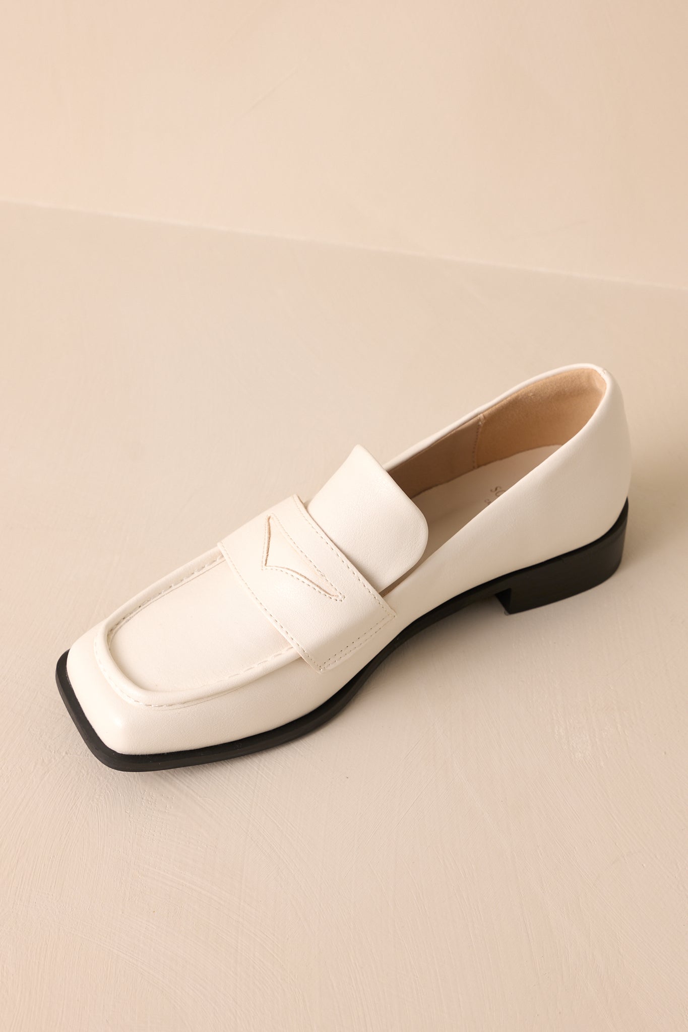 Side angled view of these white loafers that feature a slip on design, a small heel, a square toe, and a strap across the foot.