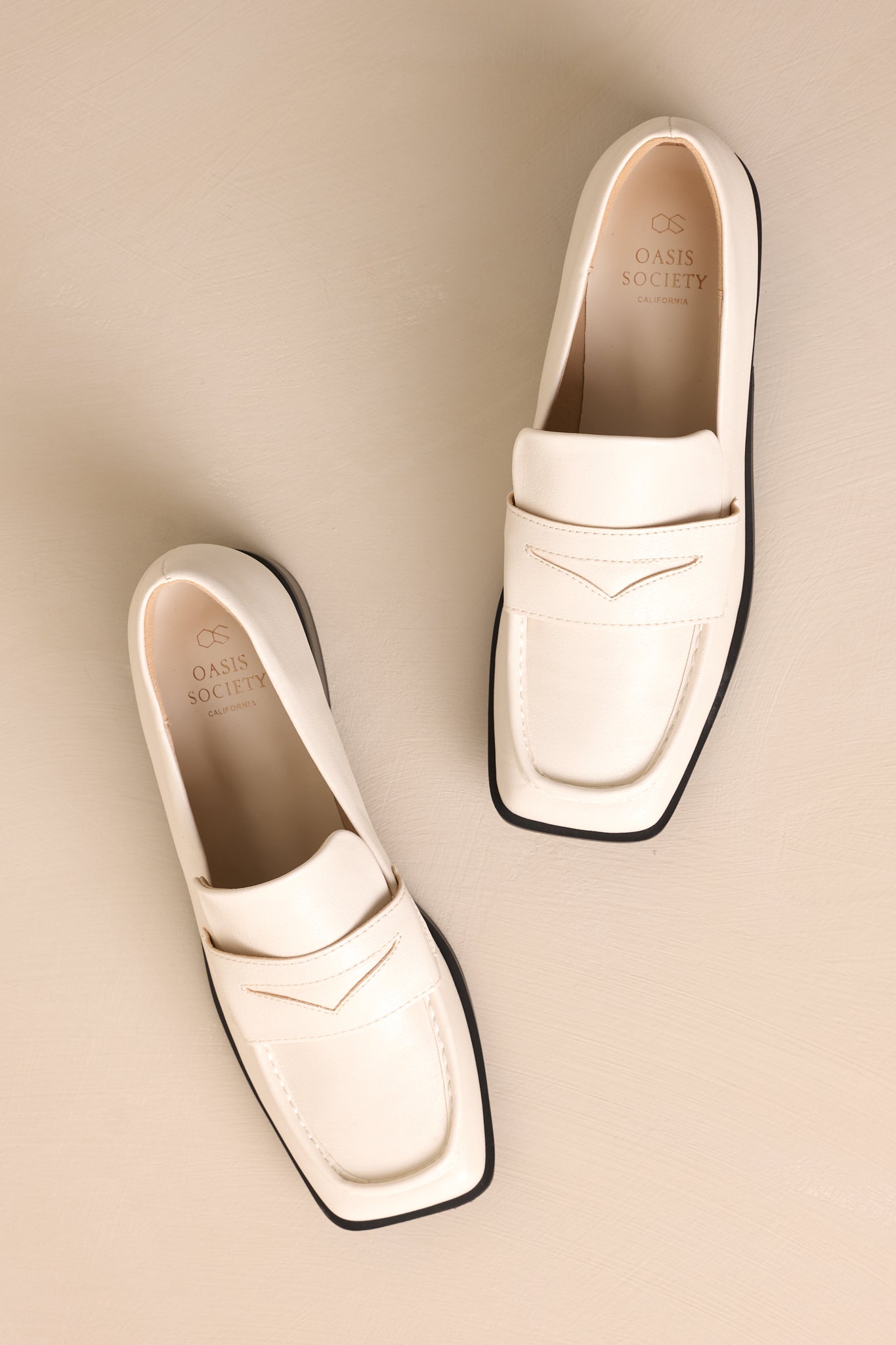 Overhead view of these white loafers that feature a slip on design, a small heel, a square toe, and a strap across the foot.