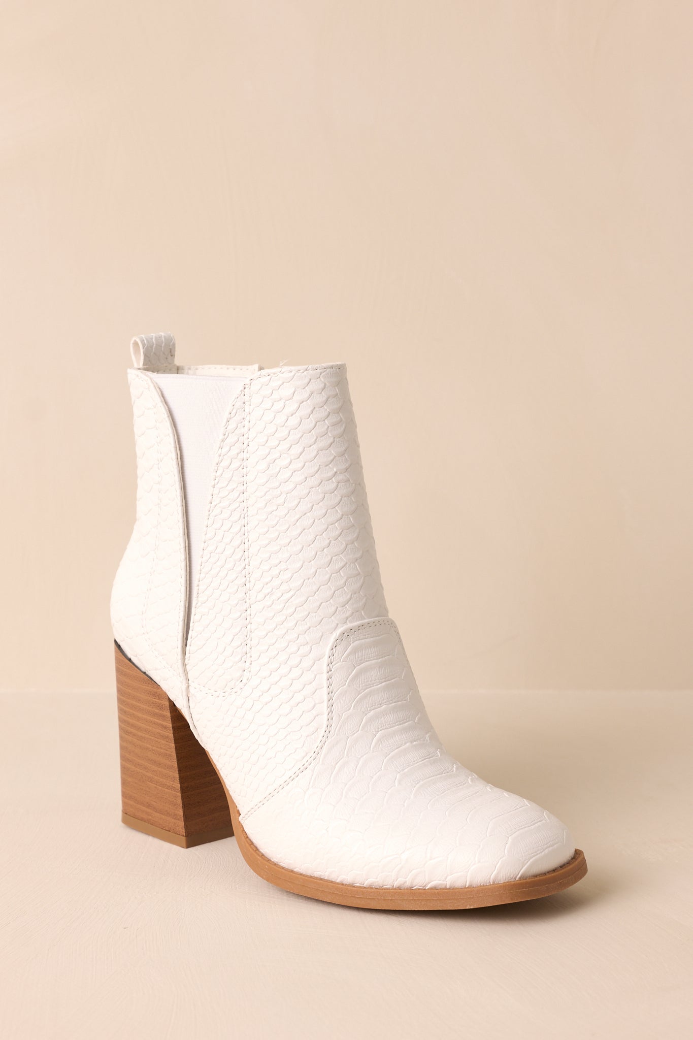 Front view of these white ankle boots that feature a square toe, a platform heel, a snake skin texture, a side zipper and an elastic side insert.