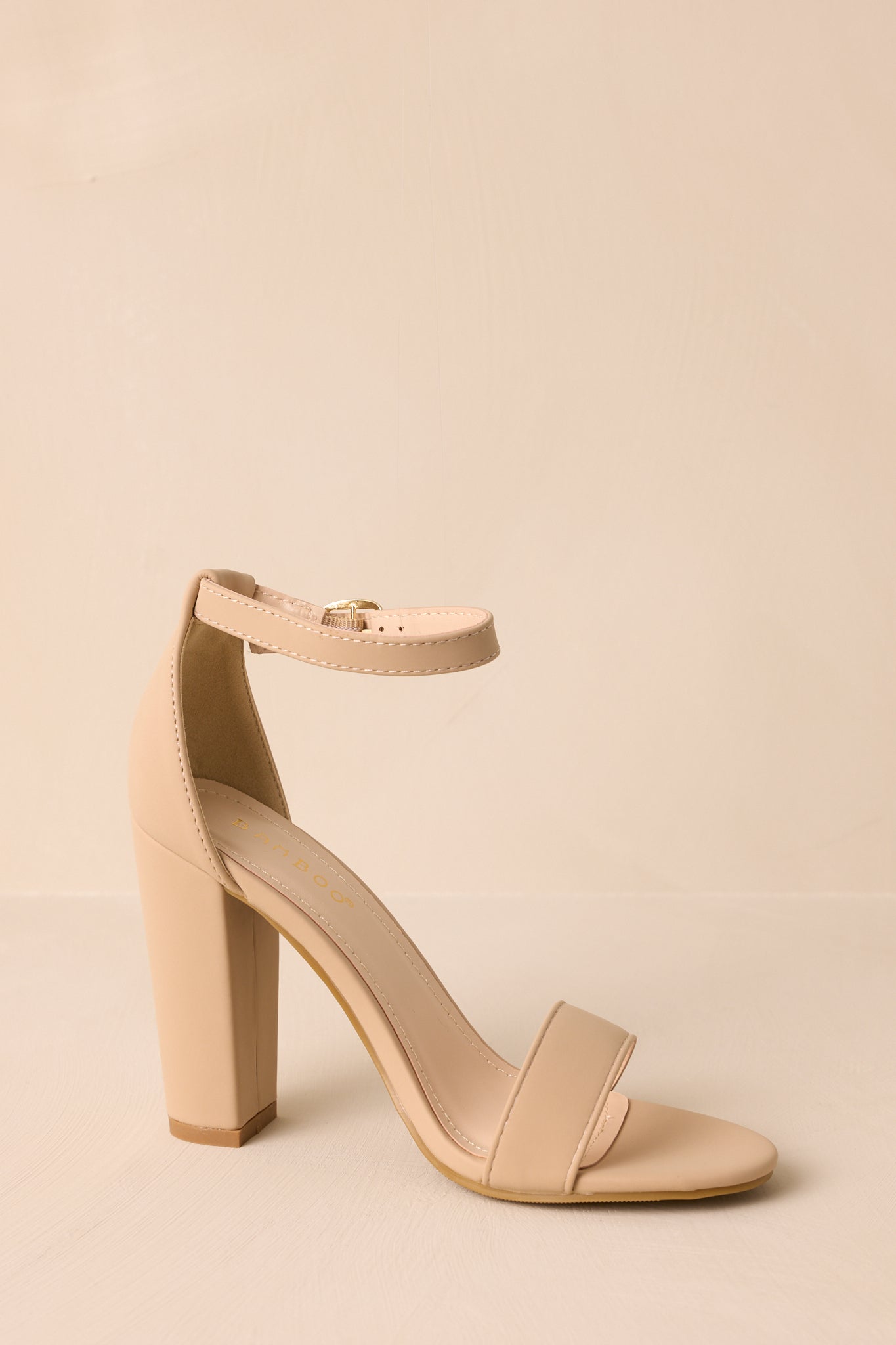 Taupe heels featuring a sleek design with an adjustable ankle strap, a wide toe strap, and a sturdy thick block heel.