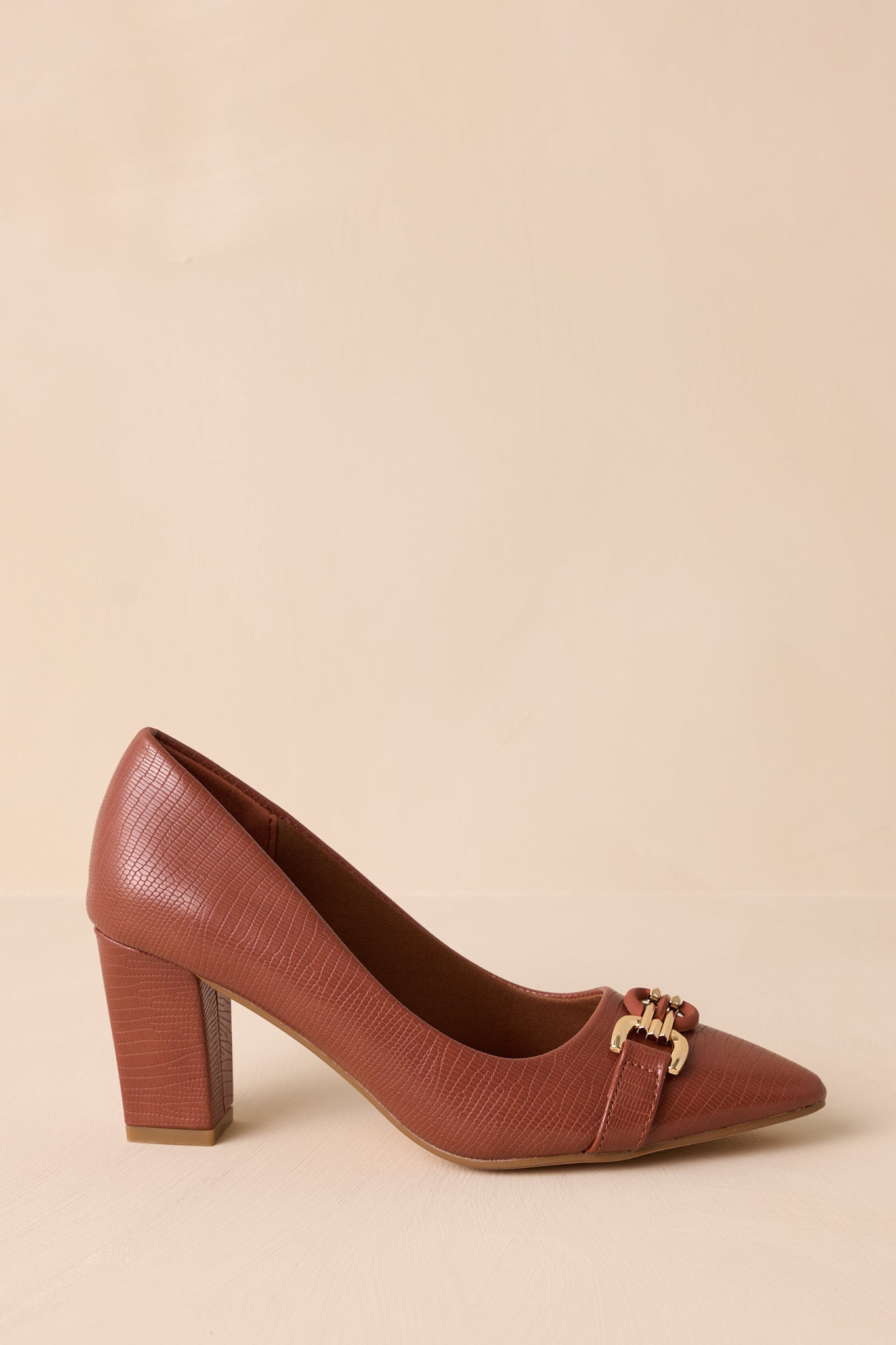 Side view of these brown heels that feature a crocodile pattern, block heel, gold hardware, and a pointed toe.