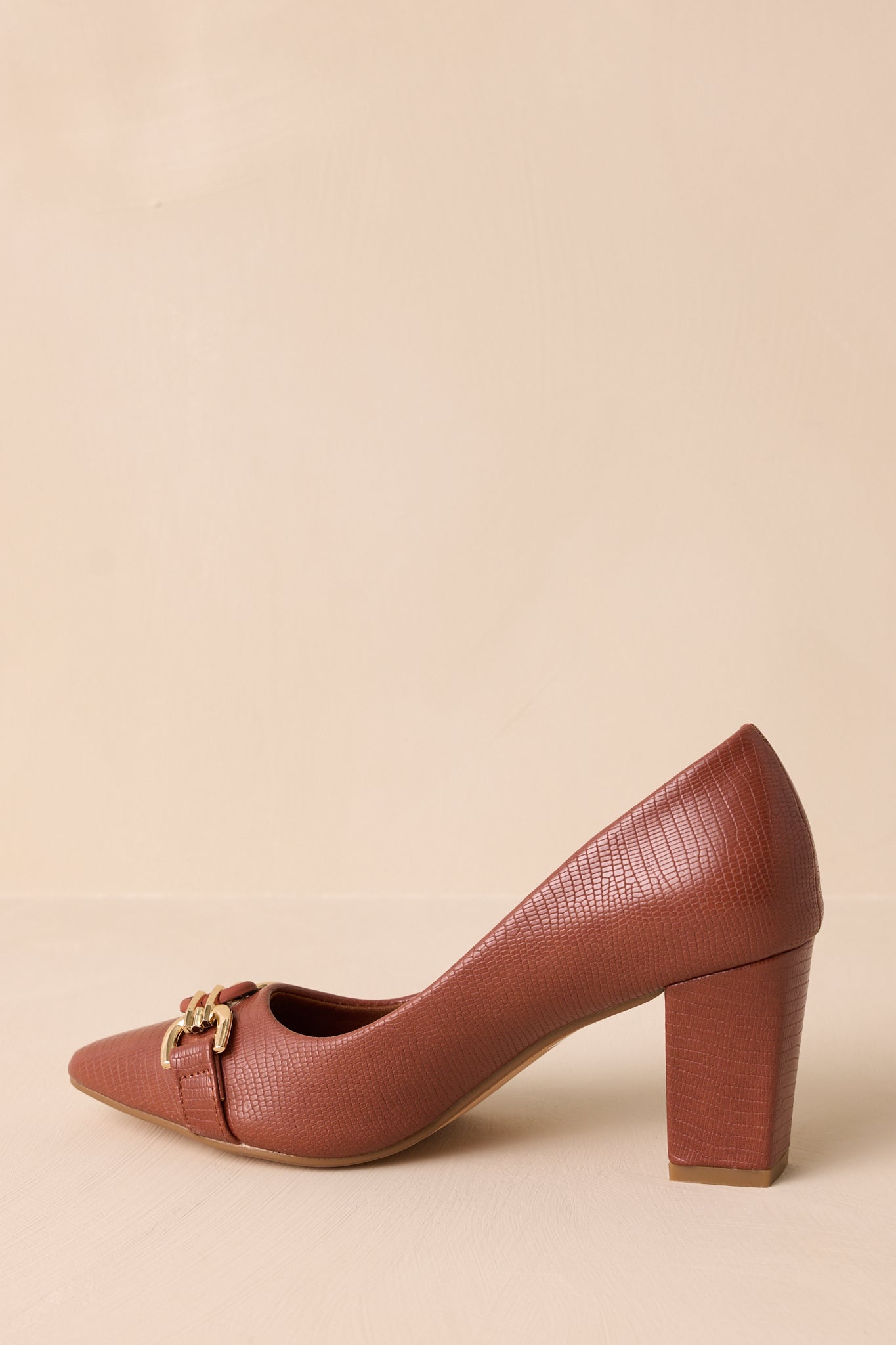 Back view of these brown heels that feature a crocodile pattern, block heel, gold hardware, and a pointed toe.