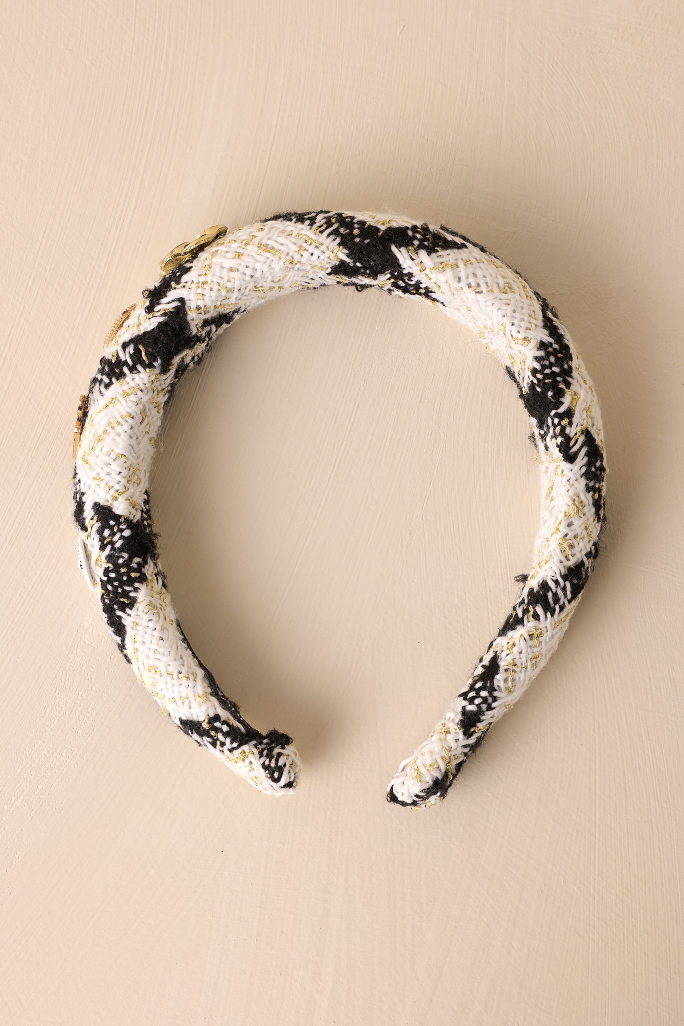 Over-head view of this headband that features a white and black tweed fabric, adorned with four adorable charms along one side. 