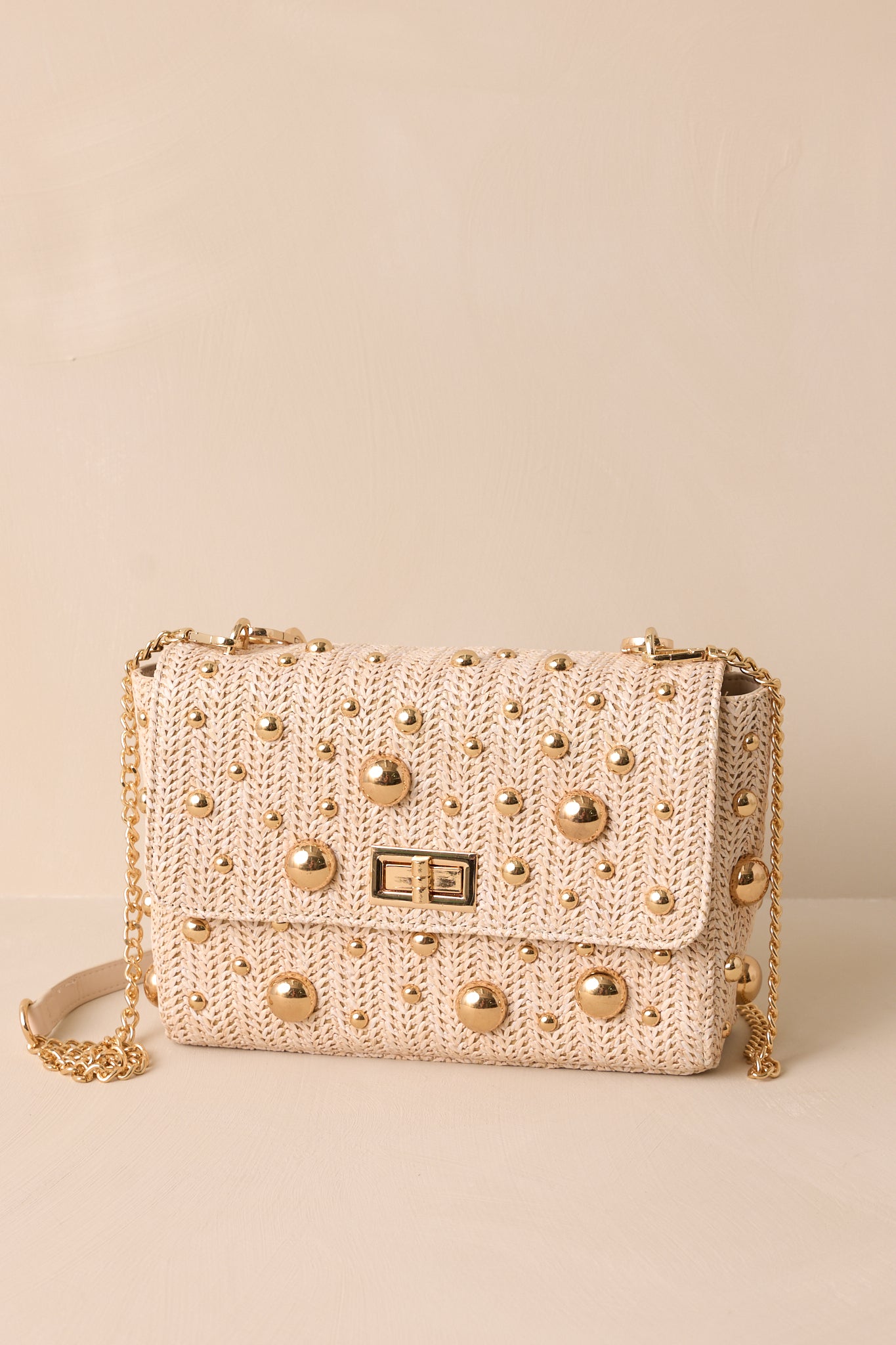 This rattan handbag features a square shape, gold reflective polka dots, a gold turn closure, gold hooks for optional strap and a zippered pouch inside.