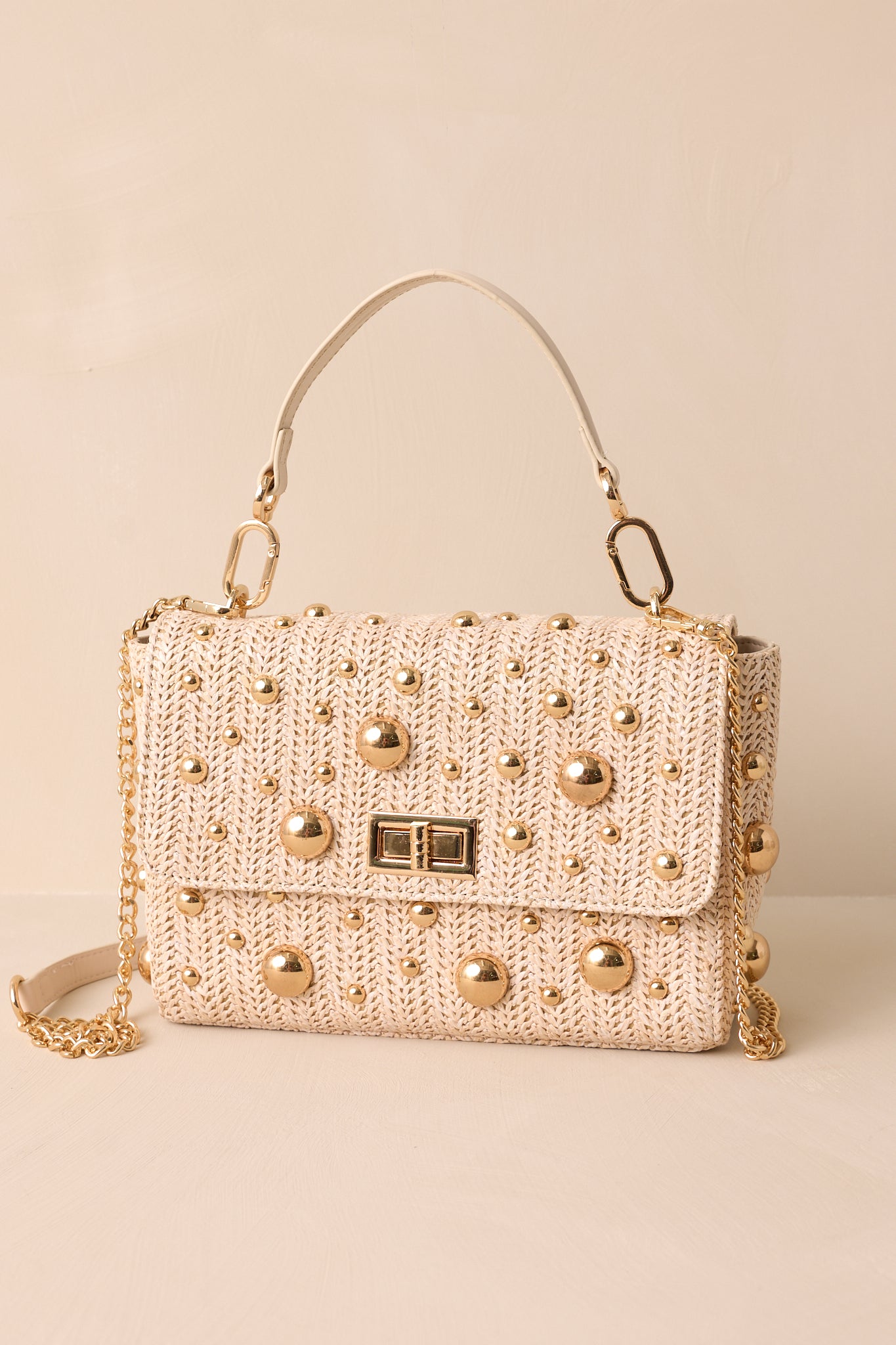 Front view of this rattan handbag that features a square shape, gold reflective polka dots, a gold turn closure, gold hooks for optional strap and a zippered pouch inside.