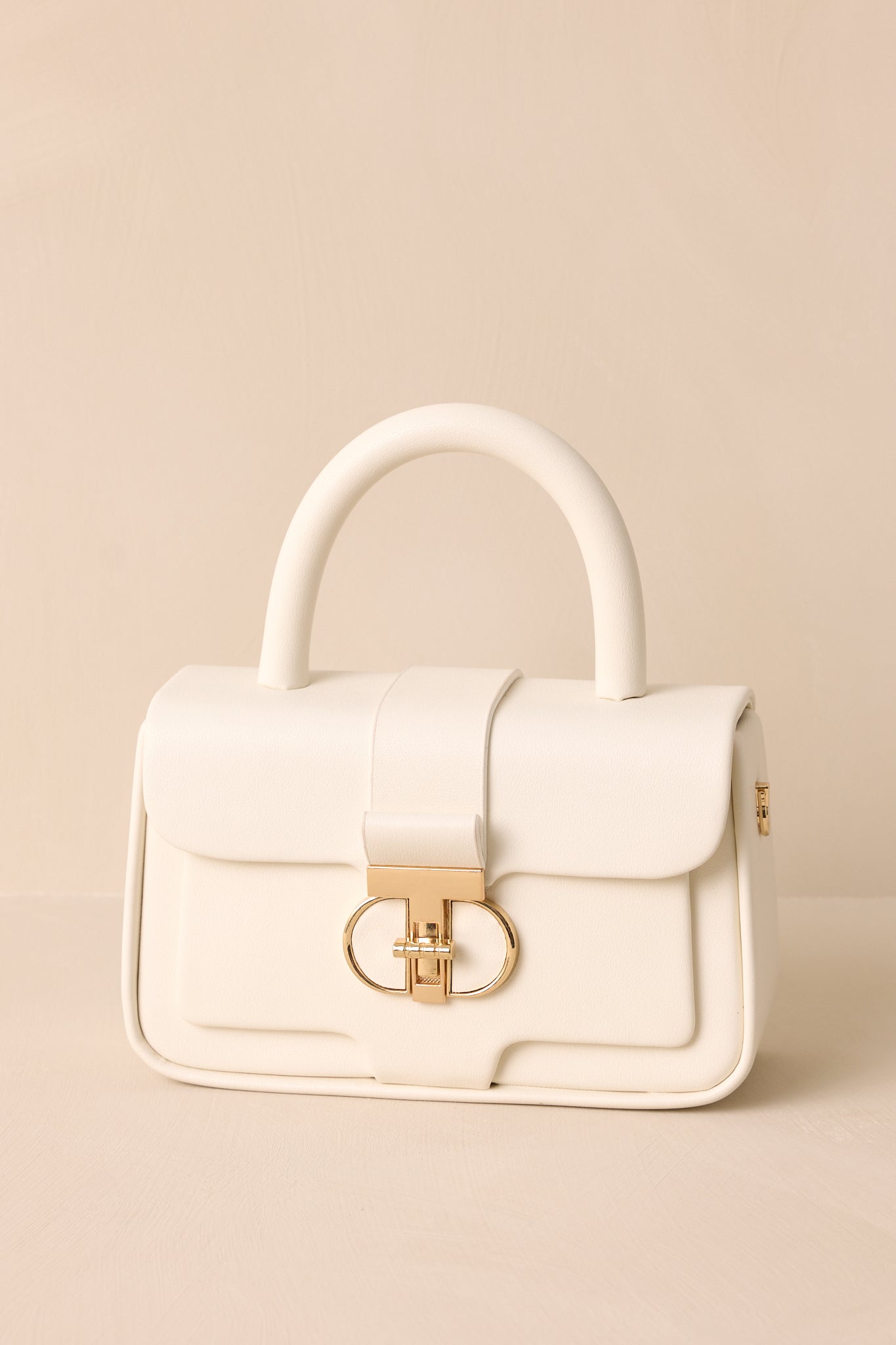 Close-up of the white handbag’s top handle, highlighting the gold hardware and the clean, minimalistic design.