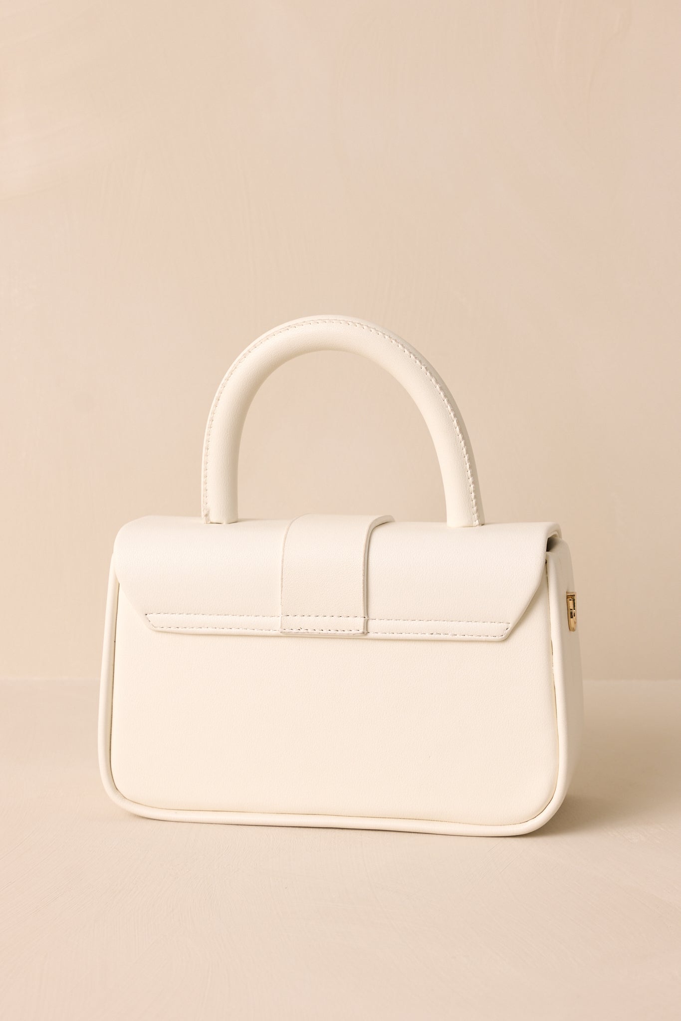 The back view of the white handbag, showcasing the clean design with gold hardware and the optional crossbody strap attached.