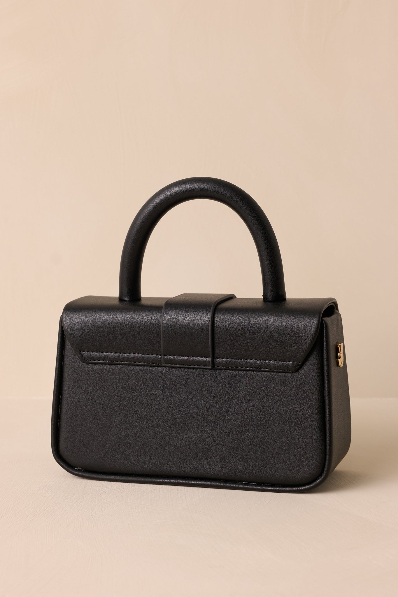 Back view of this black handbag that features a gold accent turn closure, a built in pocket, a matching mini wallet and gold accent side loops for exchangeable straps.