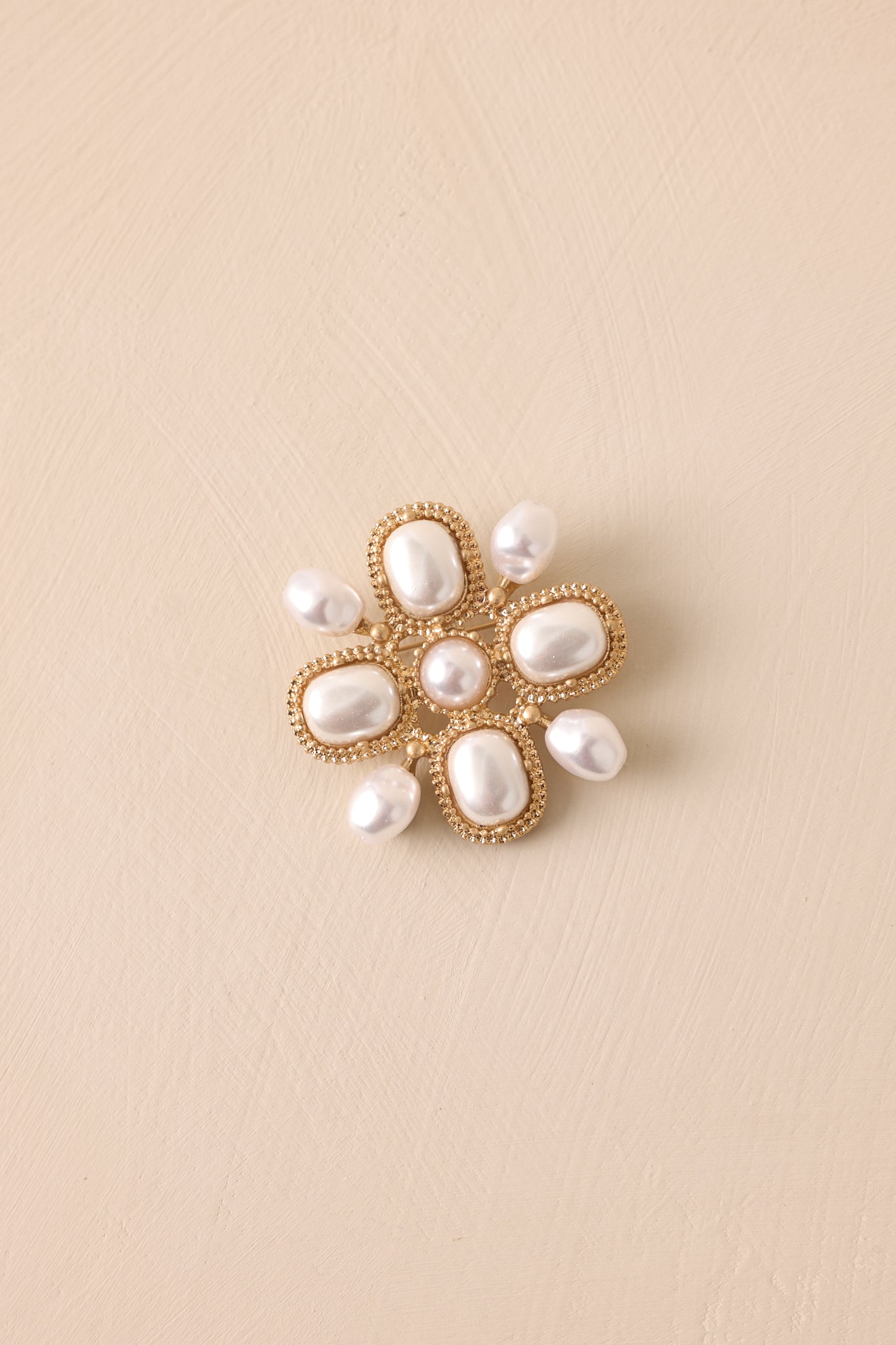 Front view of a gold brooch featuring textured gold hardware, a medium sized round faux pearl middle, four large square sections with faux pearl decorations, four little arms with one faux pearl attached to each arm and a hinge and catch closure.