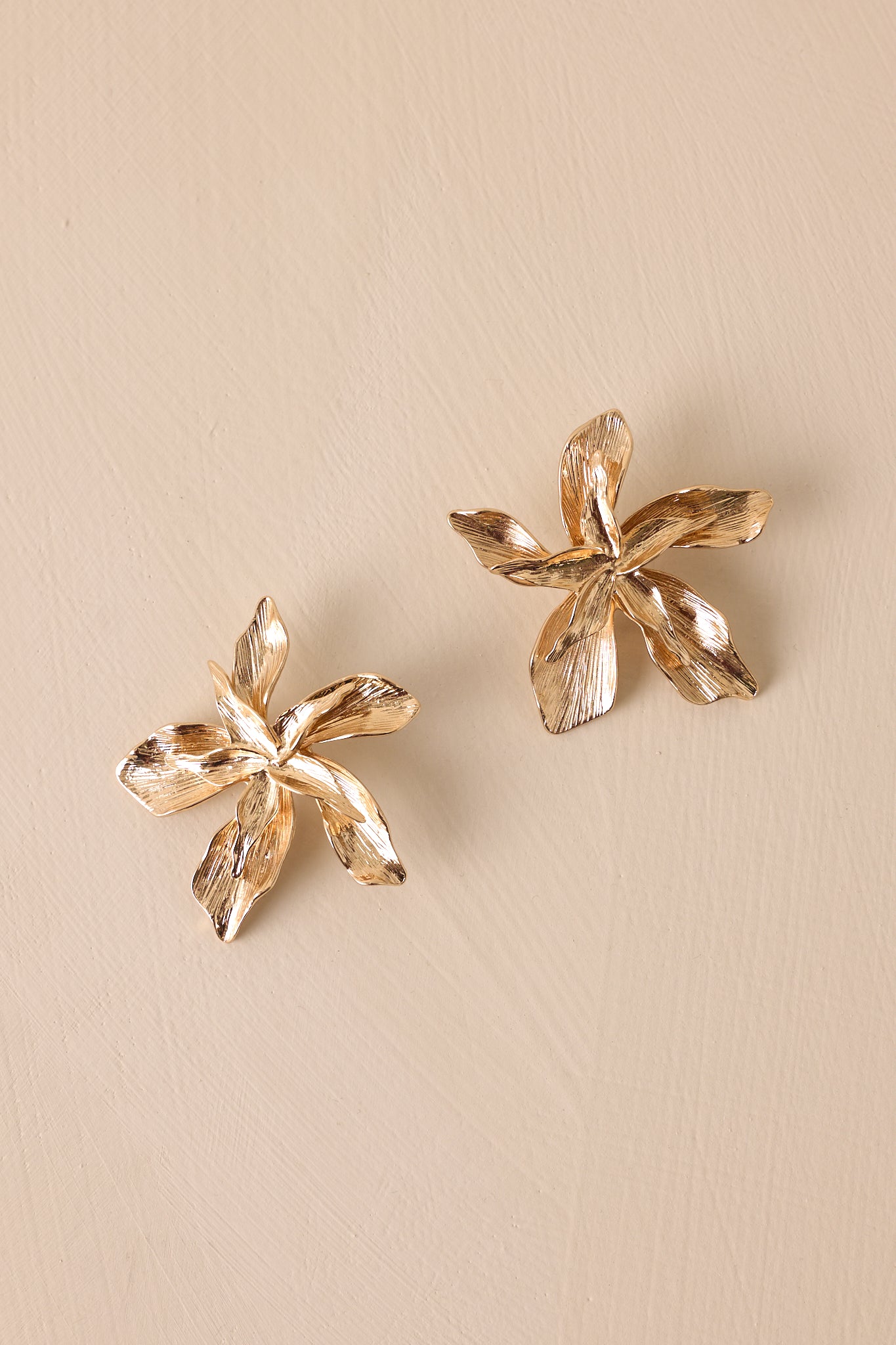 A close-up cropped shot of the gold earrings, highlighting the intricate layered floral design and the textured finish, complete with post backings.