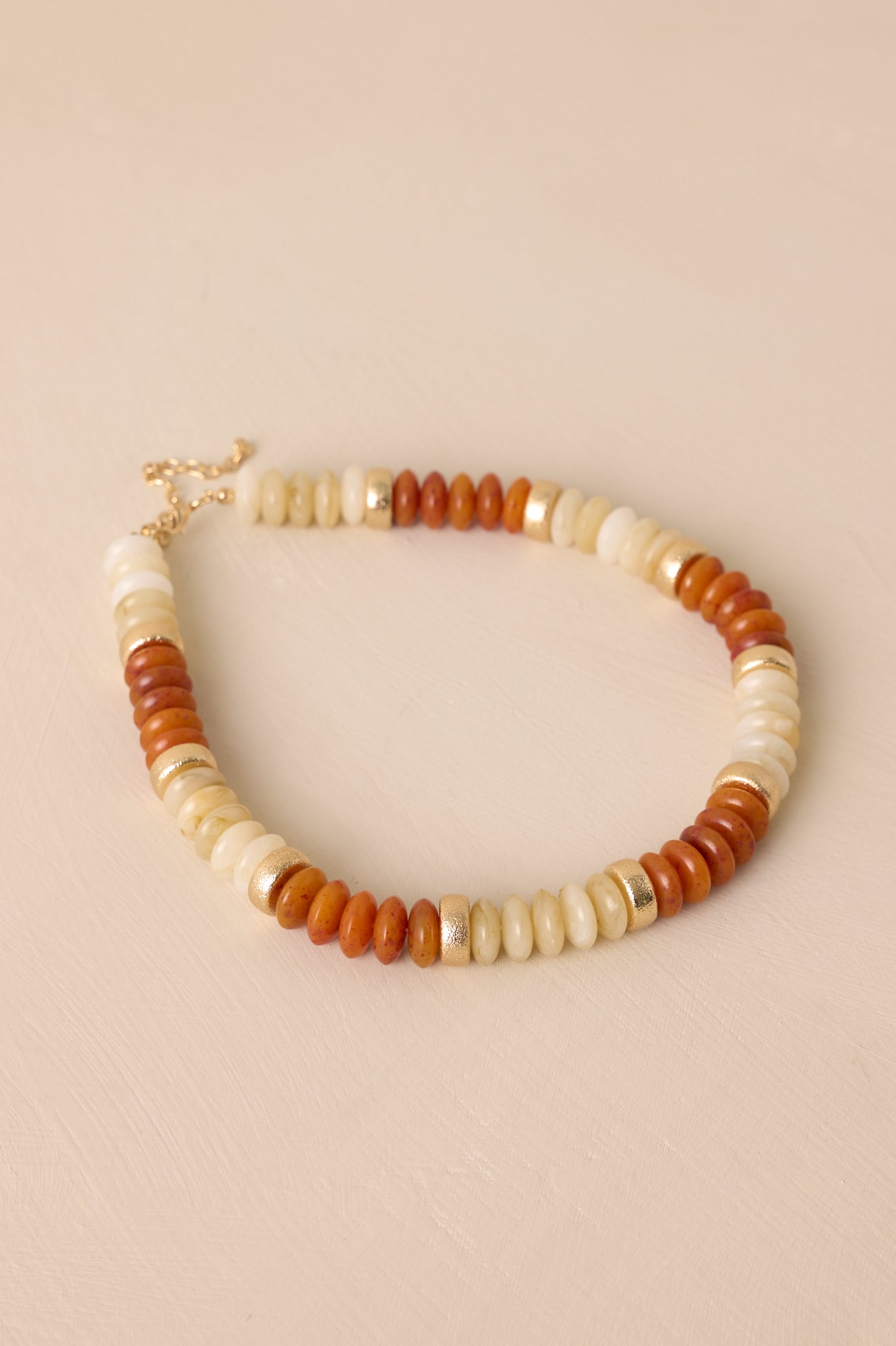 Angled view of this brown necklace that features gold hardware, ivory, gold, and brown flat beads, and a lobster clasp closure.