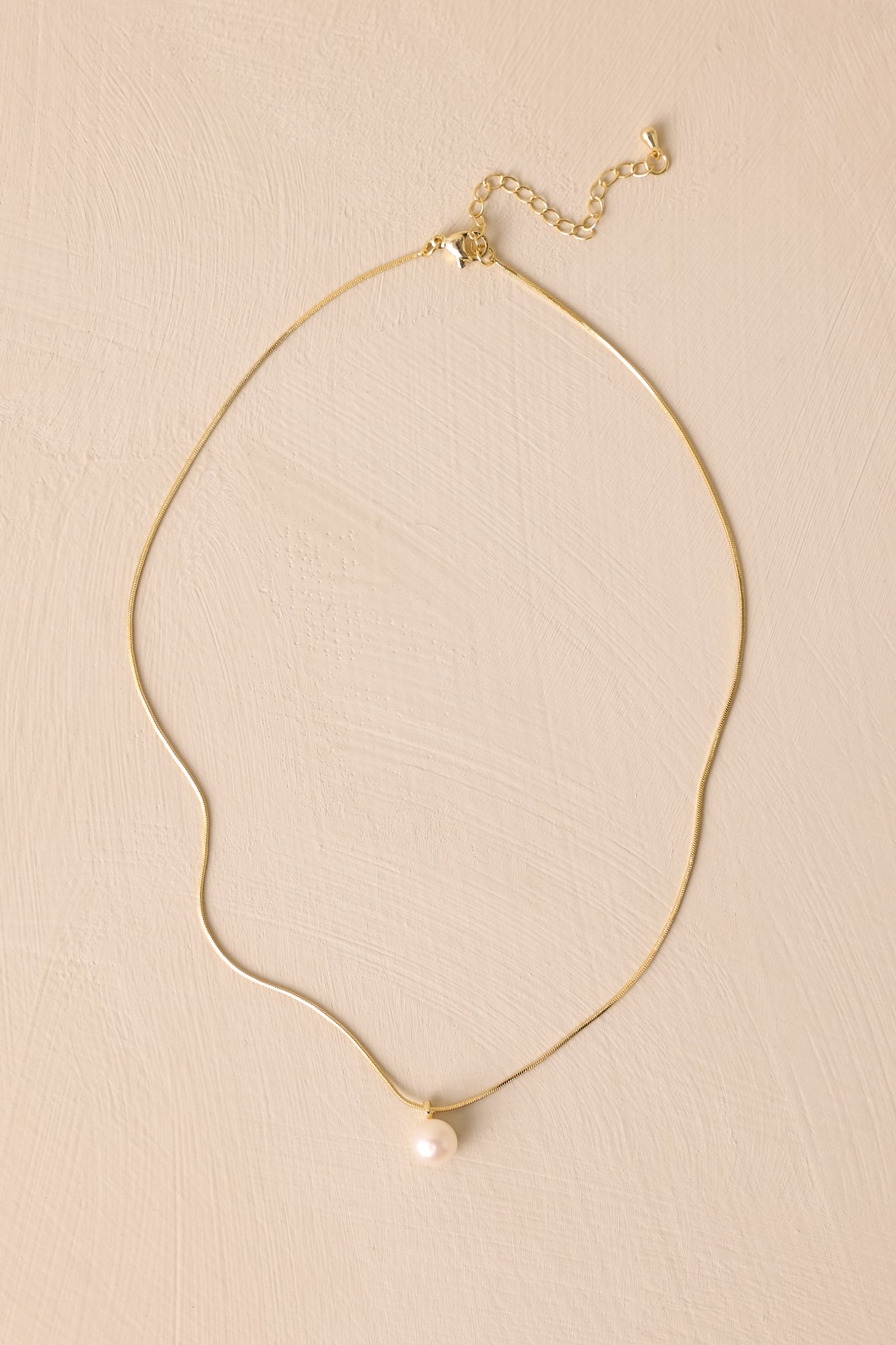 This necklace features gold hardware, a single faux pearl, and a lobster clasp closure.