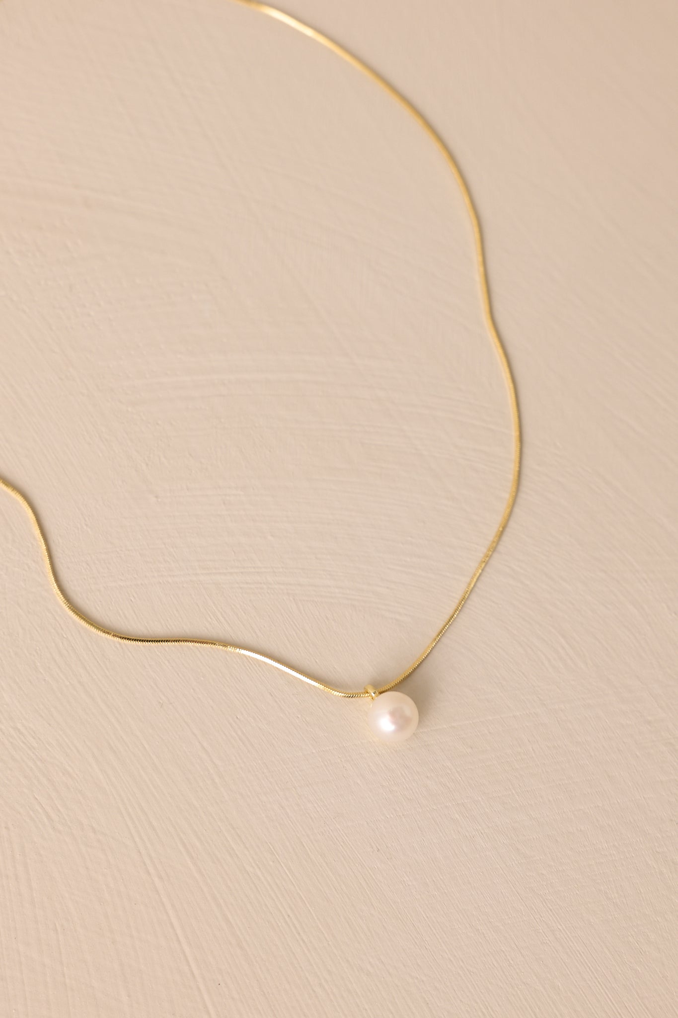 Close-up of this necklace  that features gold hardware, a single faux pearl, and a lobster clasp closure.