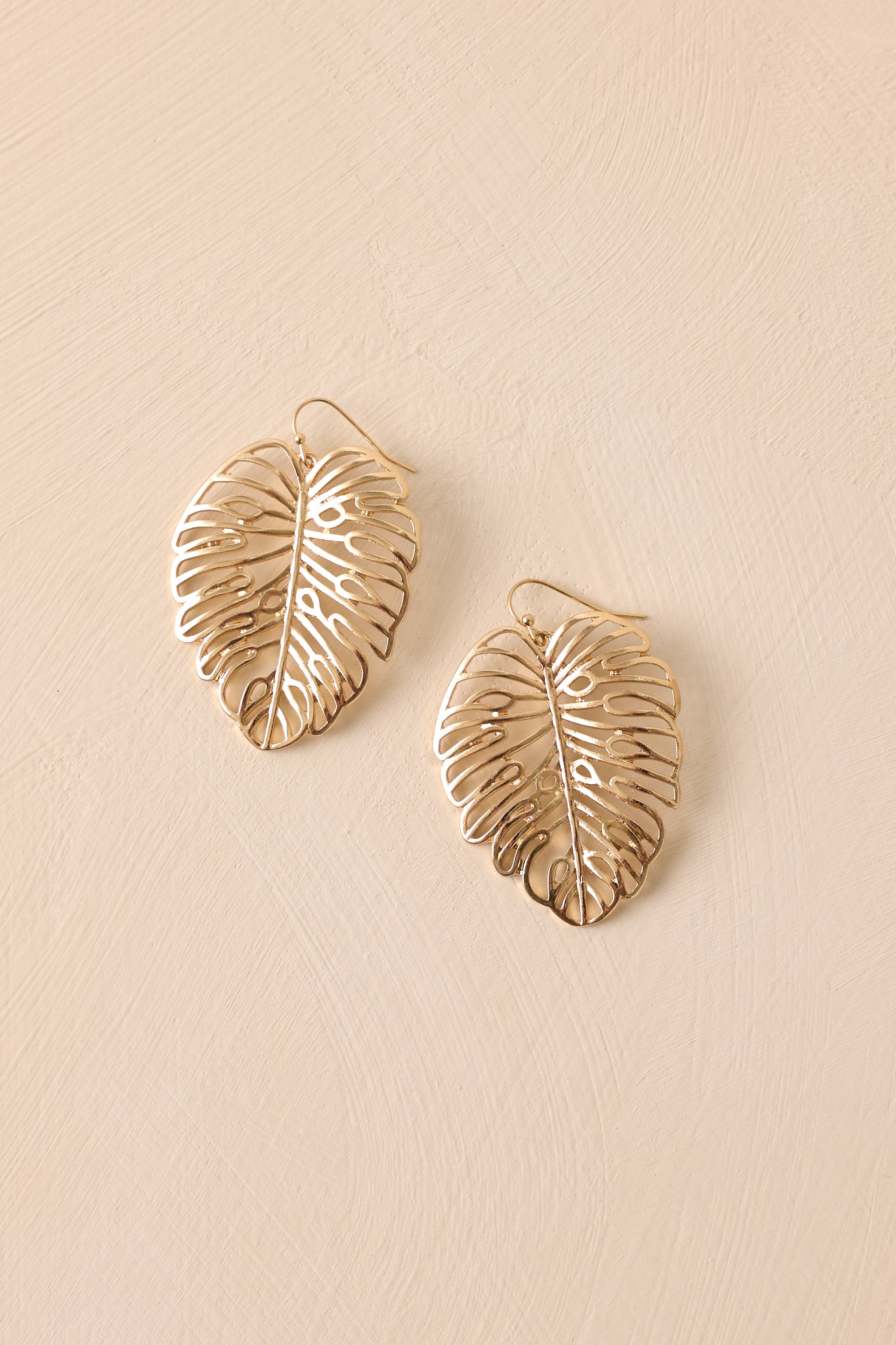 A close-up view of the gold earrings featuring transparent monstera leaf dangles. The gold hardware adds a radiant touch to the playful design.