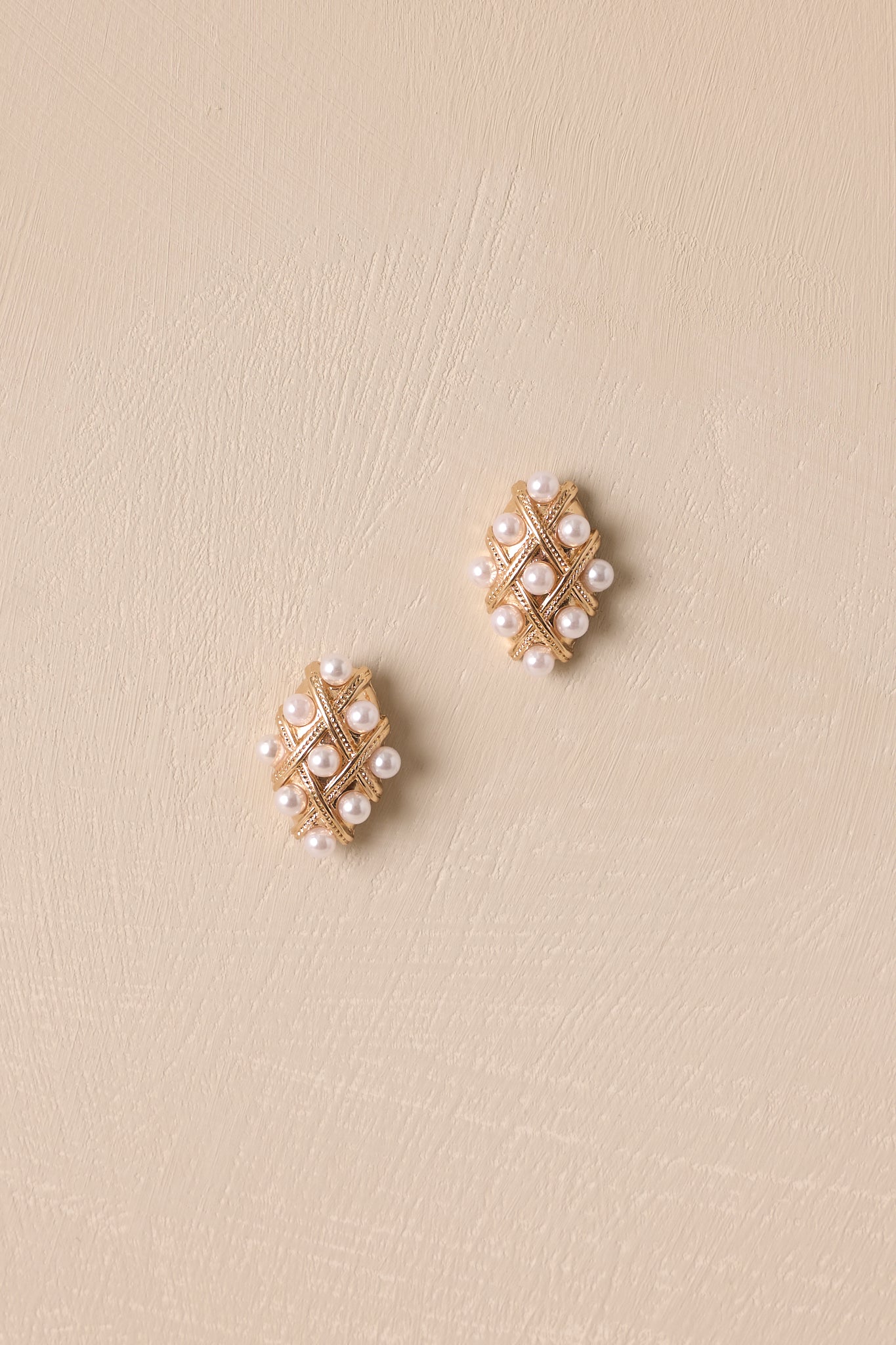 Overhead view of these gold & faux pearl earrings that feature a diamond shape, gold hardware, a quilted design, faux pearls accents and secure back postings.