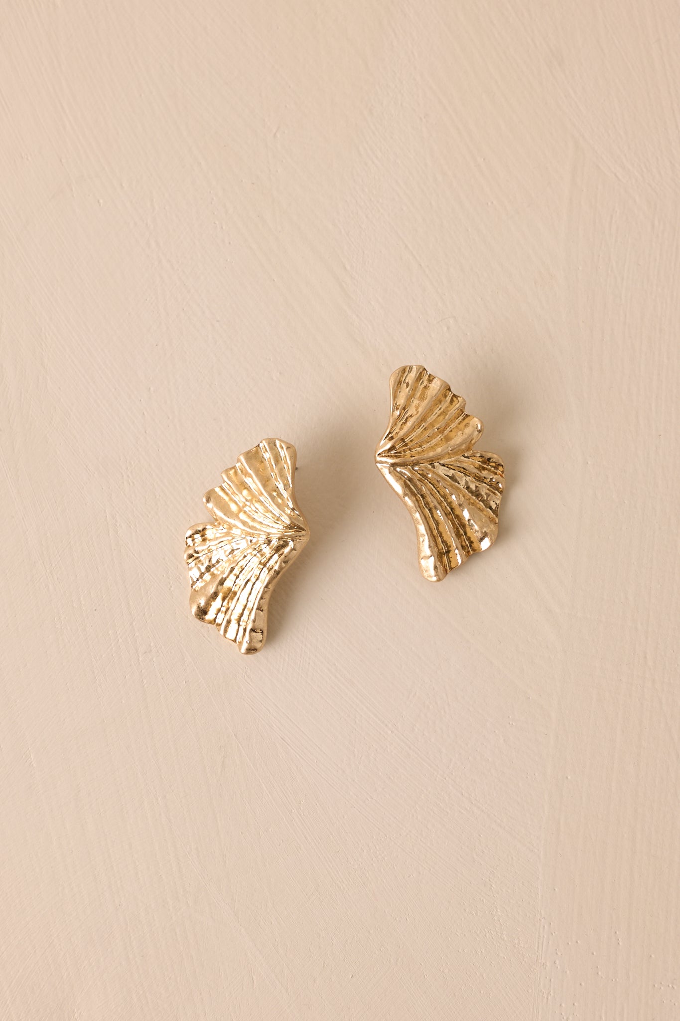 Gold earrings displayed against a beige background, showing the split bow design and intricate texture.