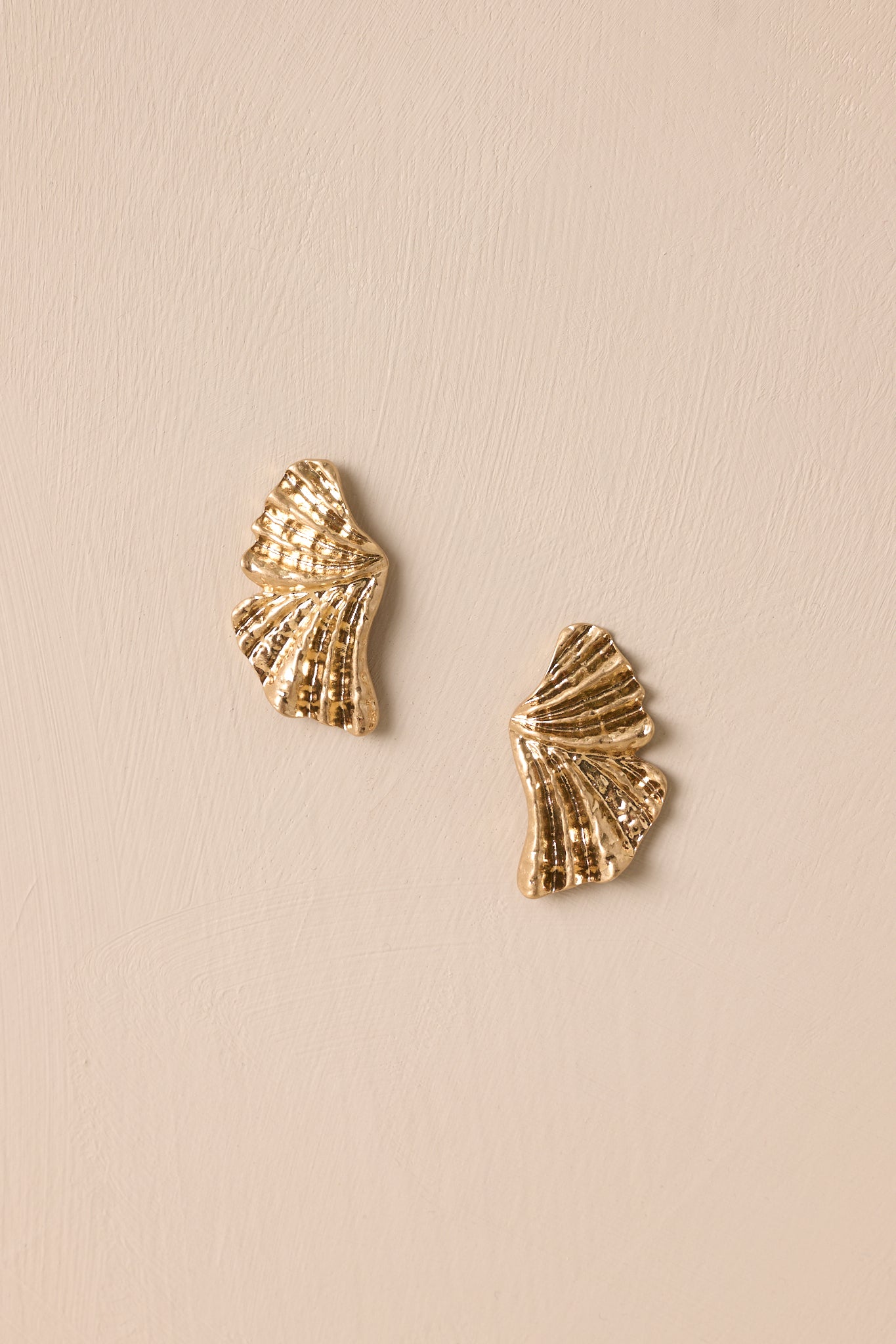 Gold textured earrings with a split bow design photographed on a beige background, emphasizing the secure post backings.