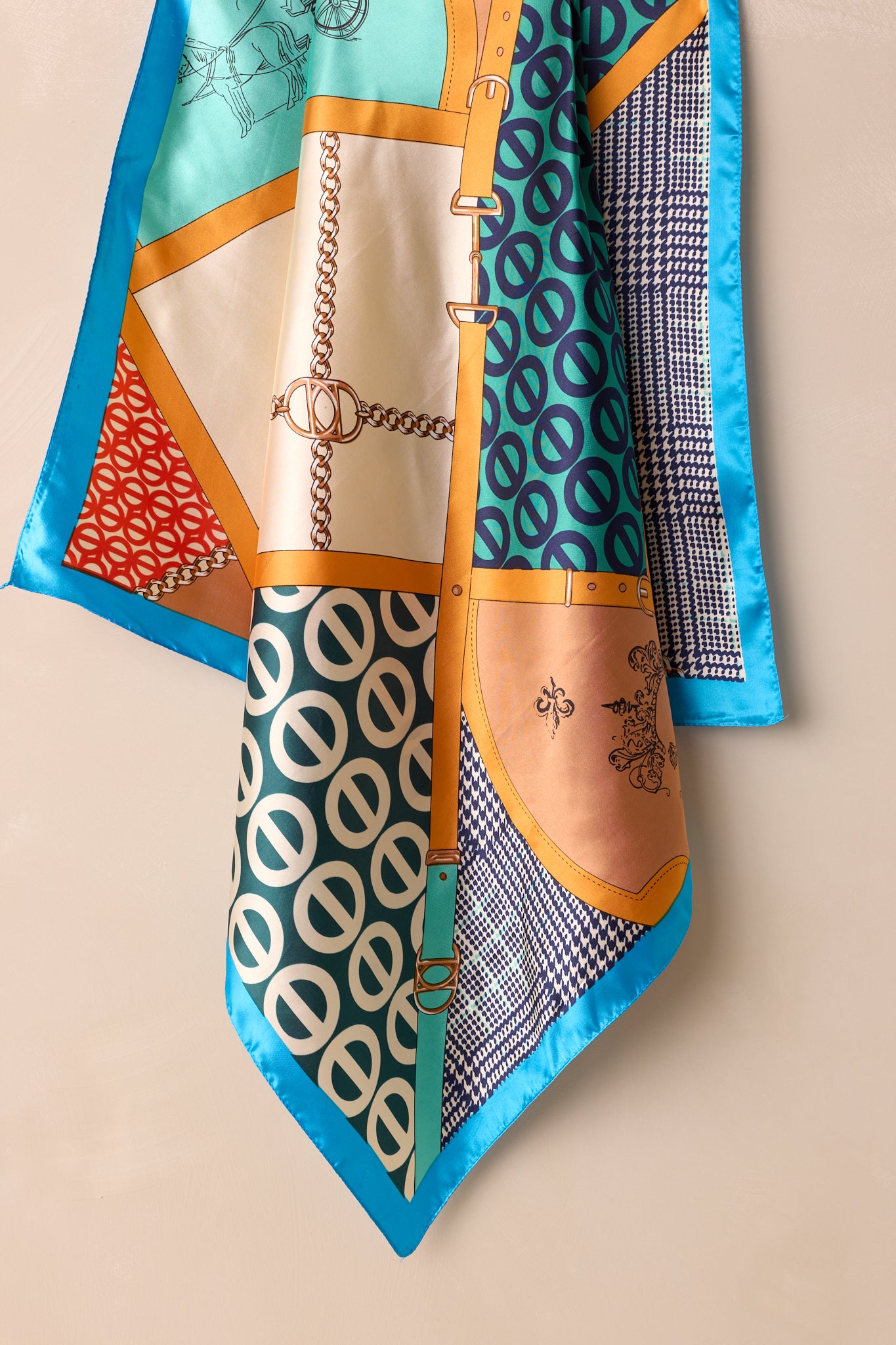 This teal blue scarf features a blue trim, with multi print designs, and a silky feel.