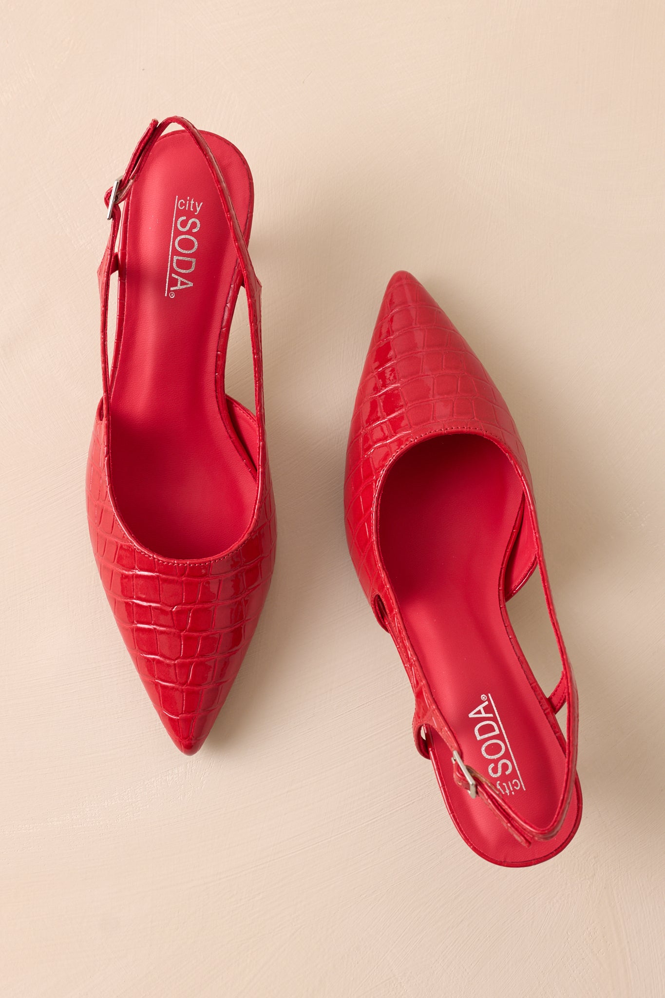 Overhead view of these red heels that feature a small gold buckle detailing, a pointed heel and small cutout detail on the side.