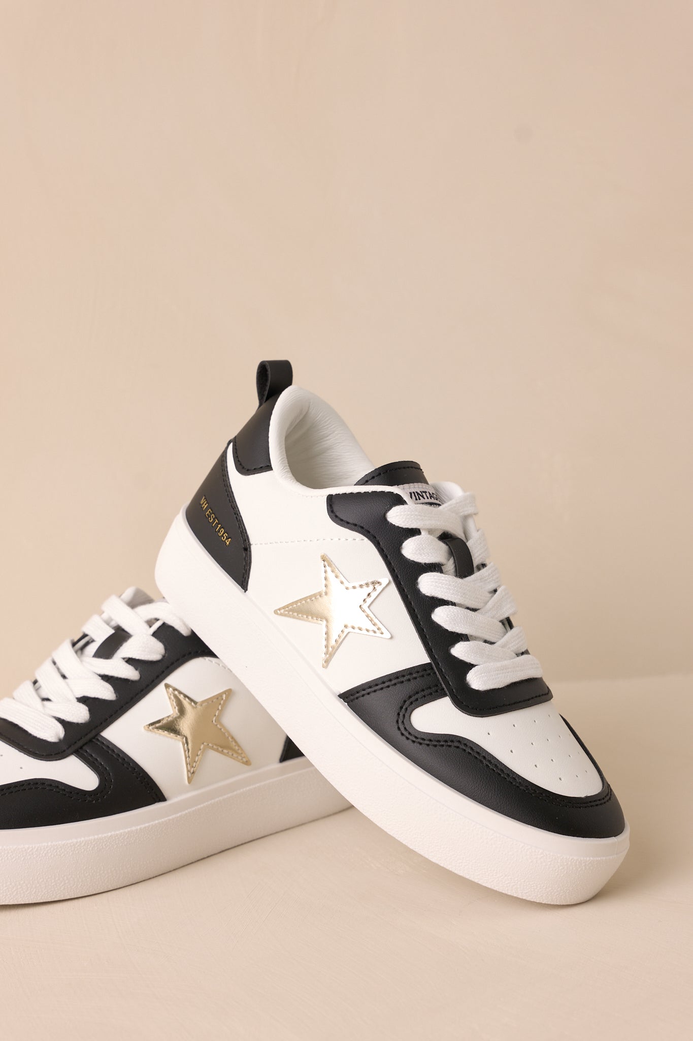 Close-up of these black sneakers that feature a rounded toe, functional white laces, interchangeable gold laces, a comfortable fit, a gold star detailing, and a thick sole.