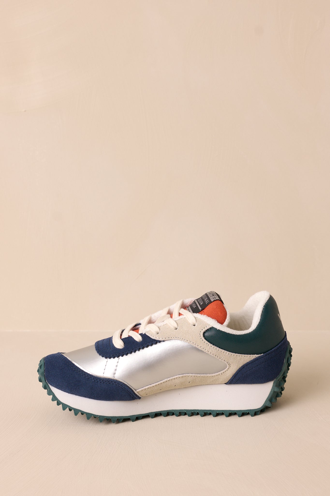 Side view of these silver sneakers that feature a rounded toe, functional laces, subtle pops of purple, navy, orange and silver, a slight platform, and a heavily textured sole.