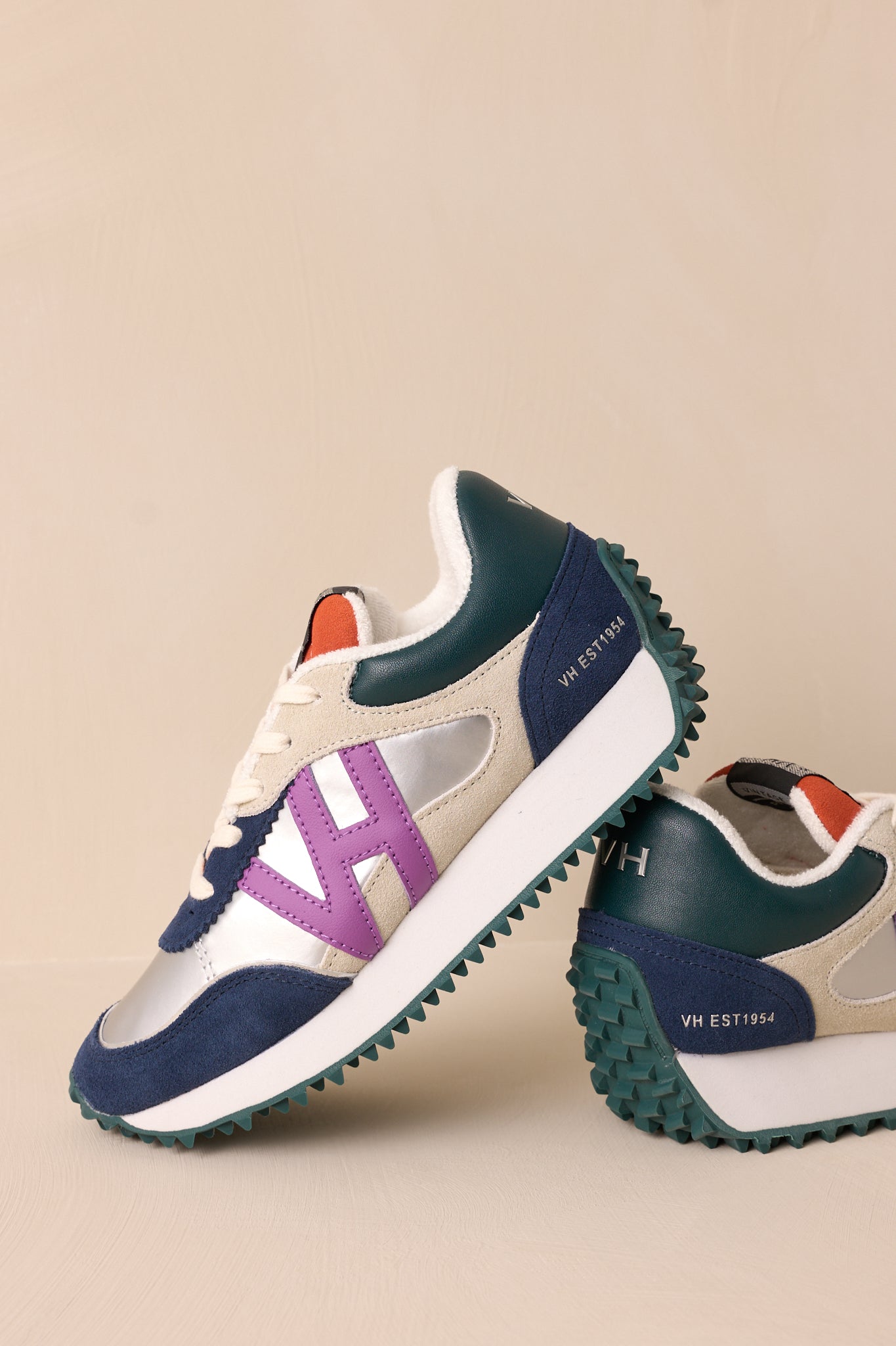 Close-up view of these silver sneakers that feature a rounded toe, functional laces, subtle pops of purple, navy, orange and silver, a slight platform, and a heavily textured sole.