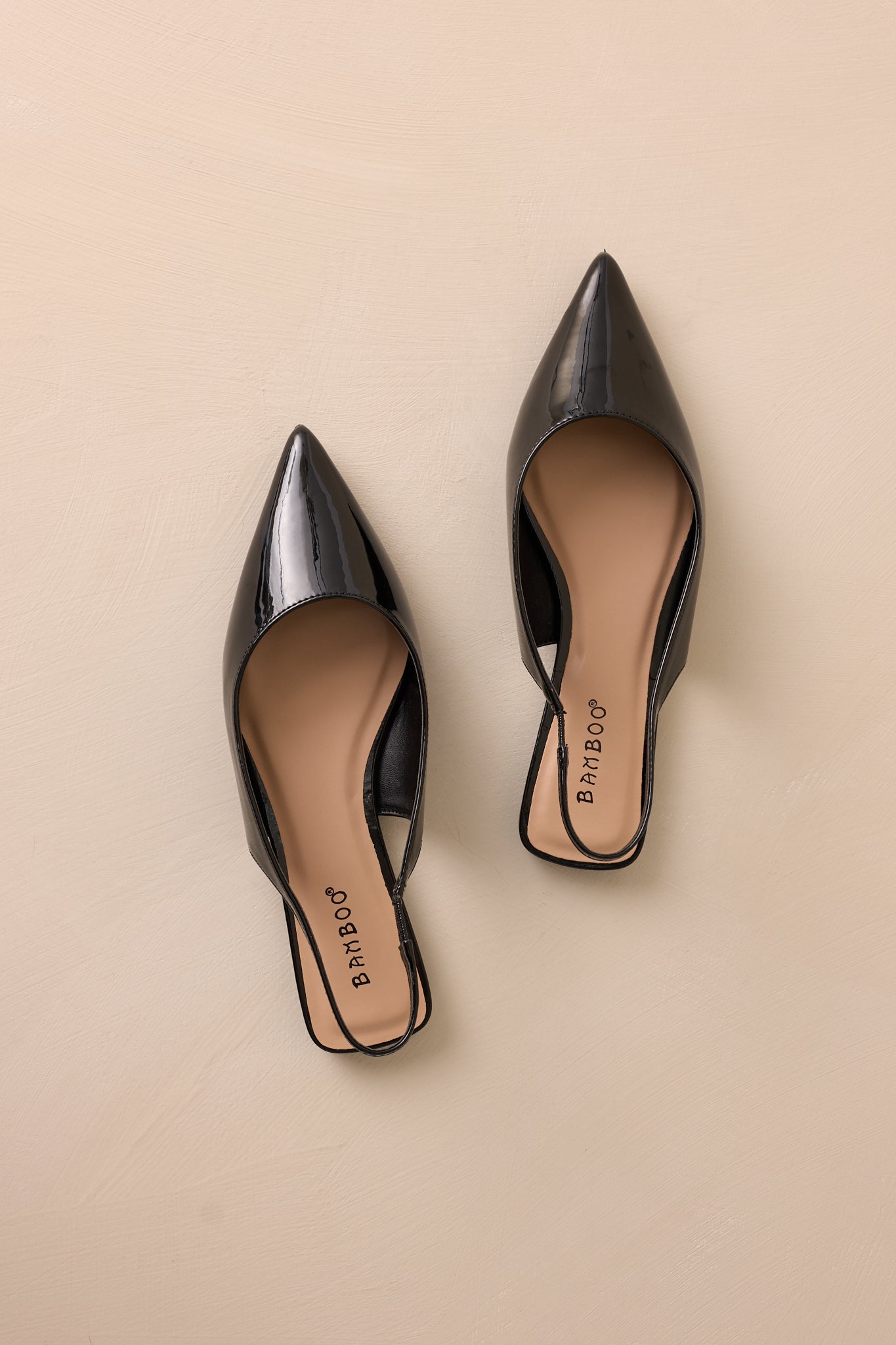 Detailed shot of the black flats showcasing the pointed toe and smooth patent finish, with the slingback strap visible.