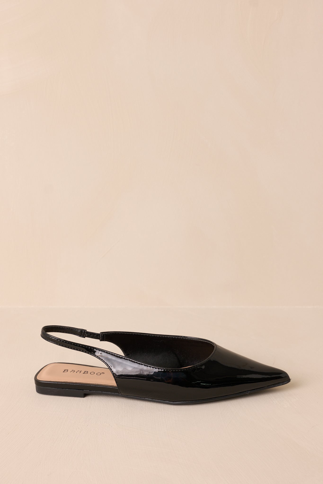 Close-up of black flats with a pointed toe and a glossy patent finish, highlighting the sleek design.