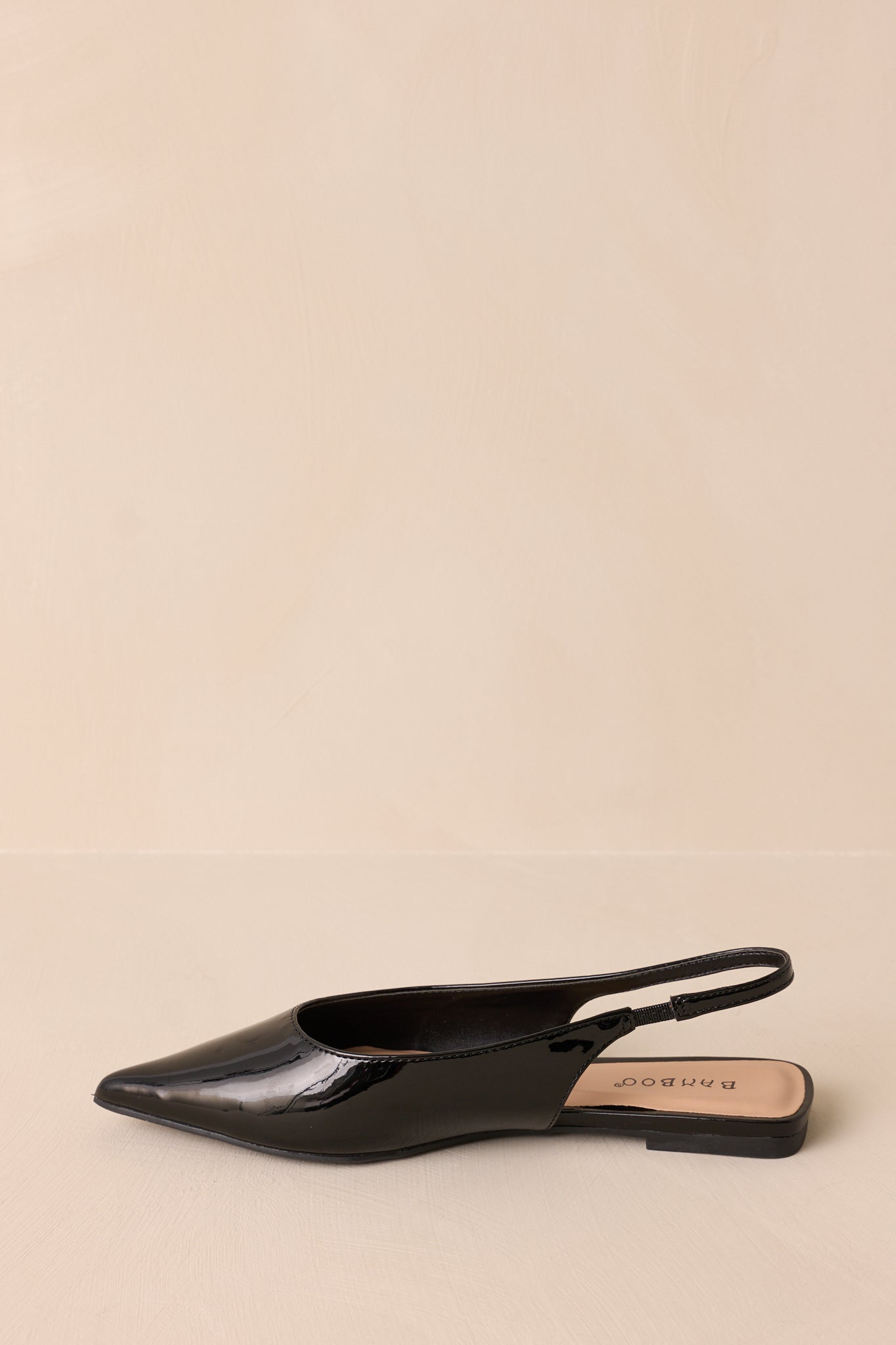 Detailed shot of the black flats showcasing the pointed toe and smooth patent finish, with the slingback strap visible.