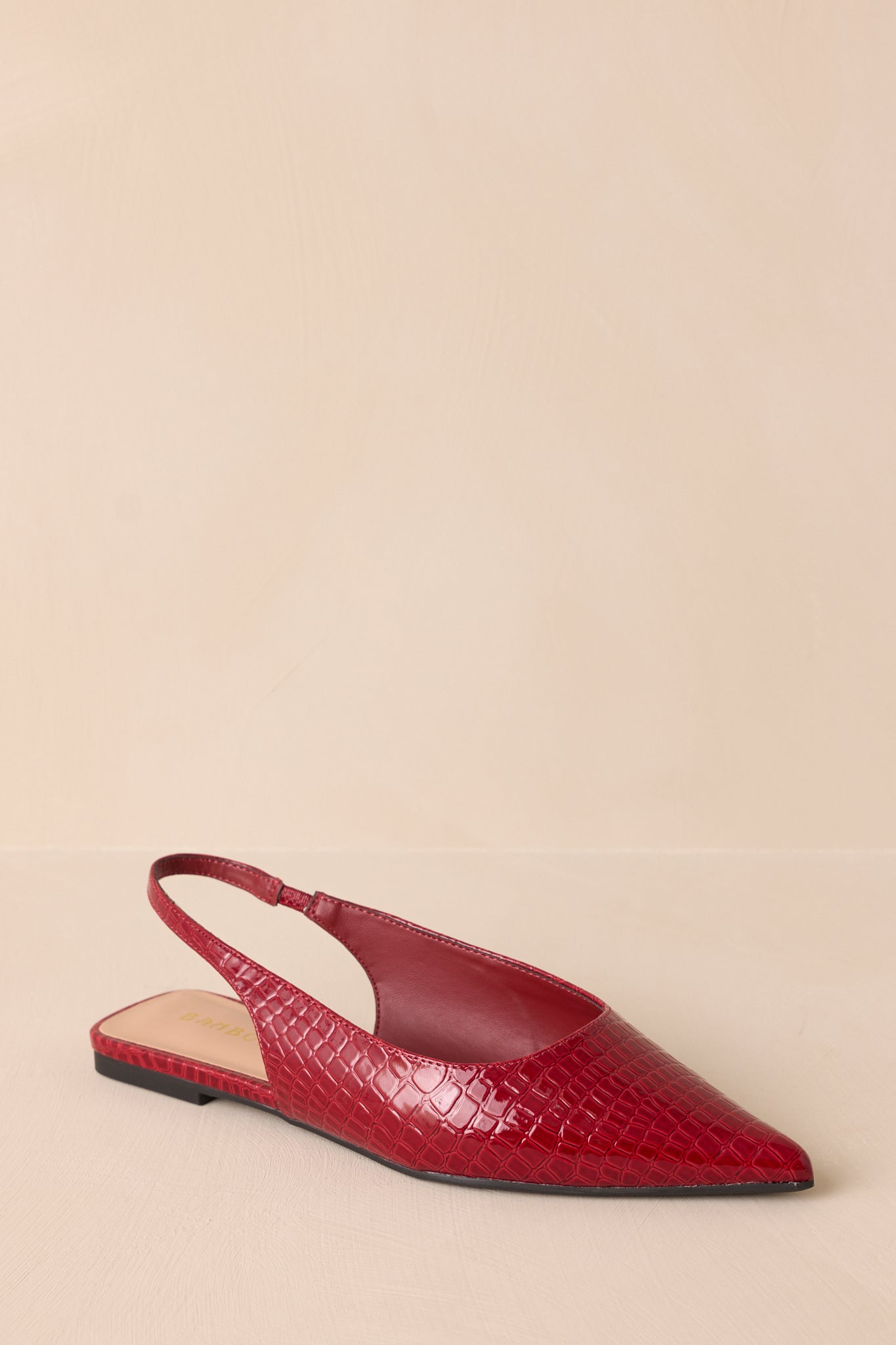 These red flats feature a pointed toe, a faux crocodile leather, a slingback-style strap, and a sleek red color.