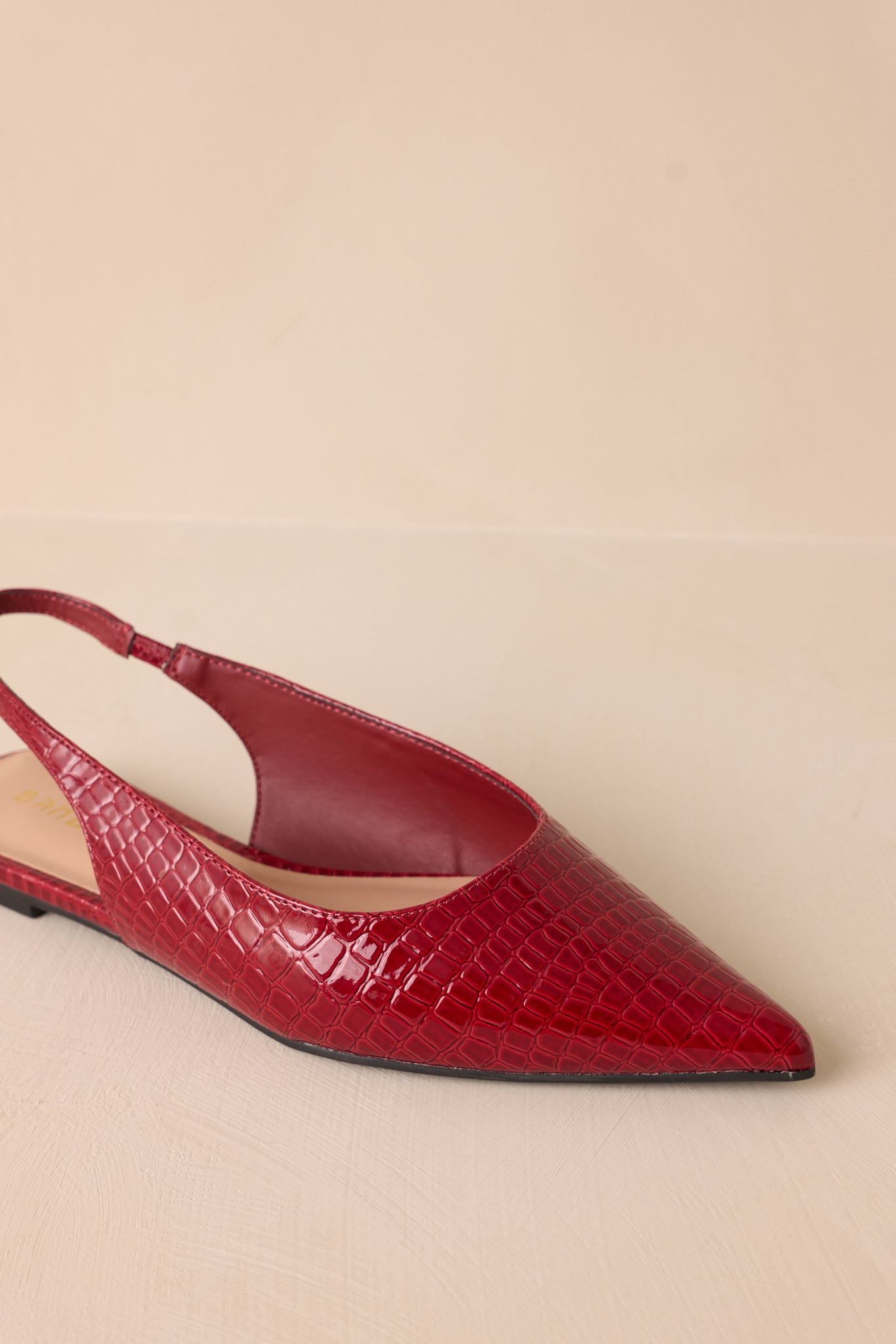 Close up view of these red flats featuring a pointed toe, a faux crocodile leather, a slingback-style strap, and a sleek red color.