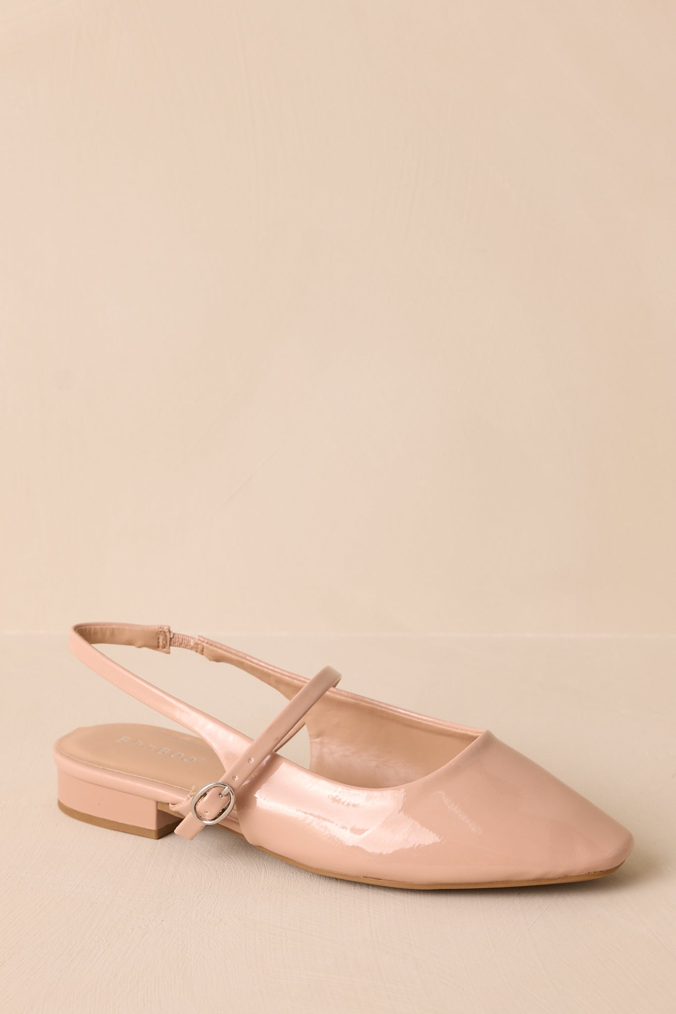 Angle view of the beige flat, emphasizing the patent finish and the sleek silhouette of the shoe.