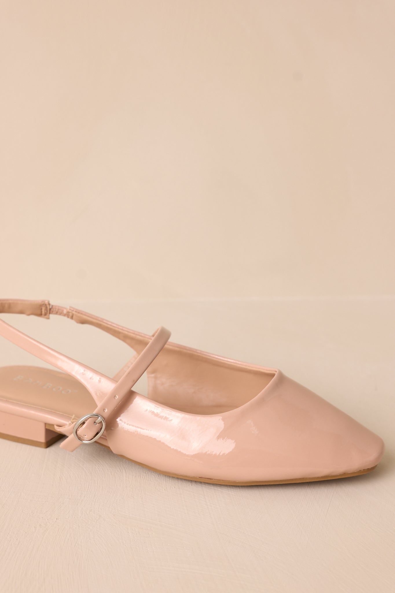 Close-up of the across-the-foot strap, focusing on the silver buckle and the glossy patent finish of the beige flats.