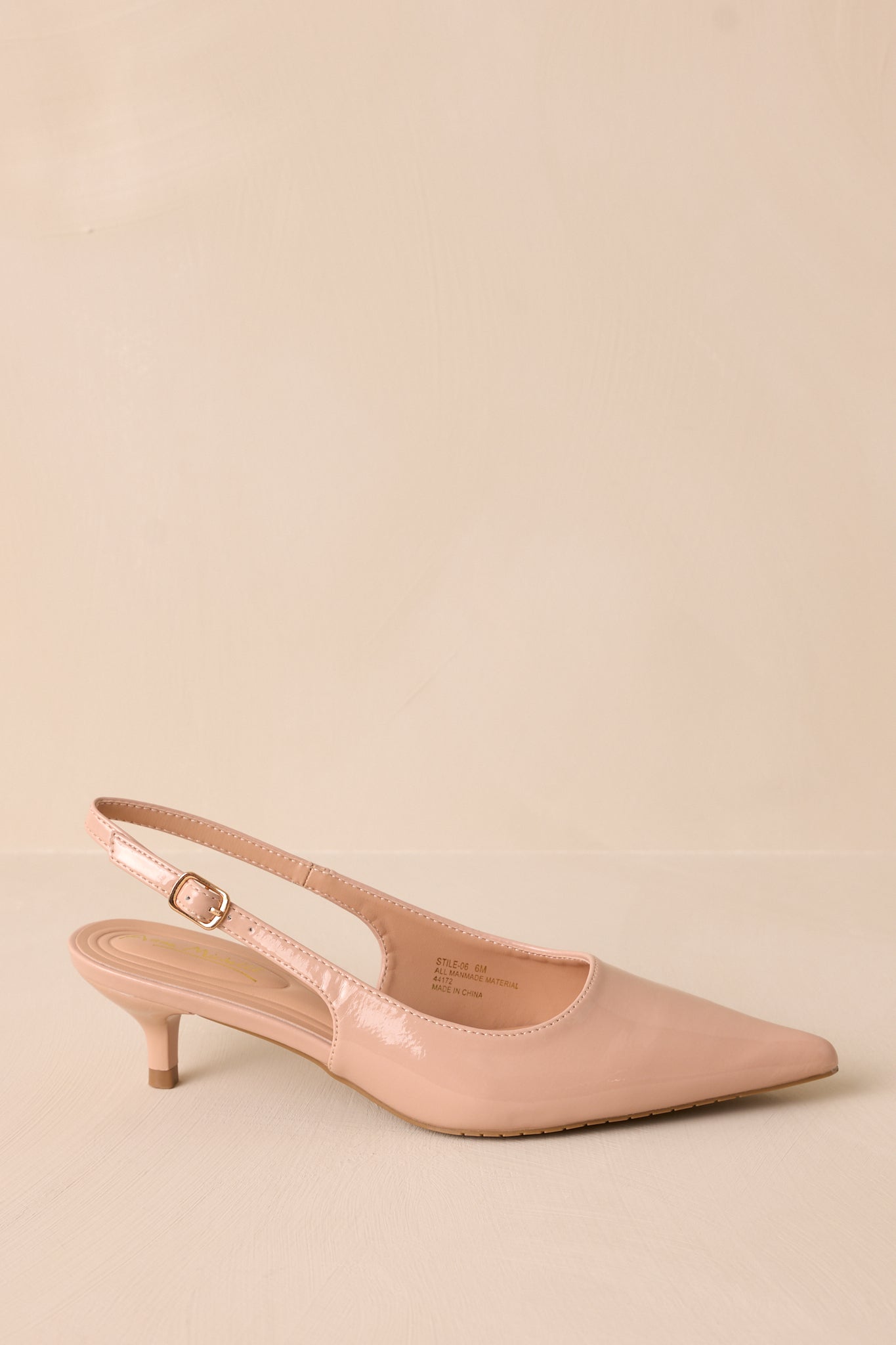 Side view of a single nude patent heel with a pointed toe, adjustable slingback strap, and short kitten heel.