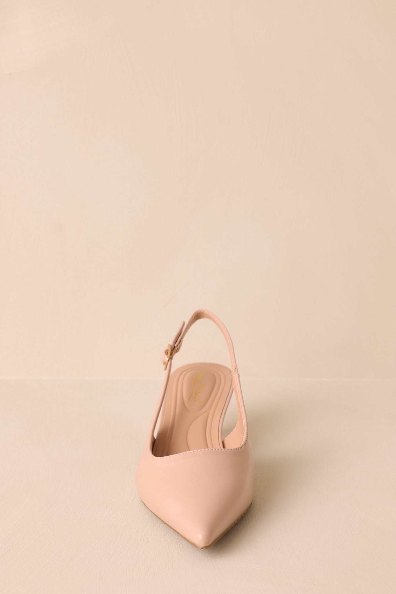 Front view of a nude patent heel with a pointed toe and slingback strap. The glossy material and cushioned insole add a sleek, polished look to the short kitten heel design.