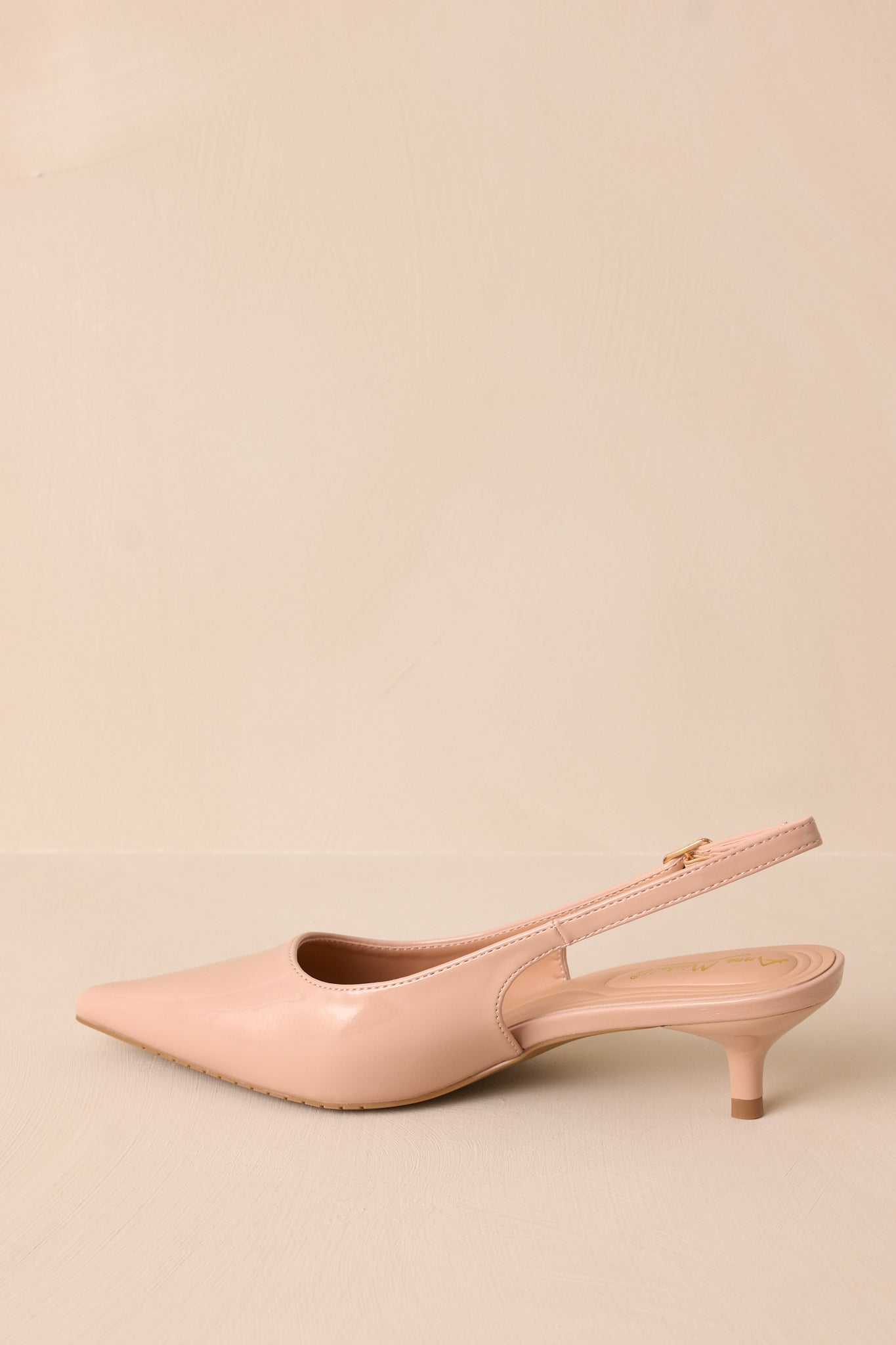 Side profile of a nude patent heel with a pointed toe and slingback strap. The gold buckle and short kitten heel highlight the shoe’s chic and comfortable design.