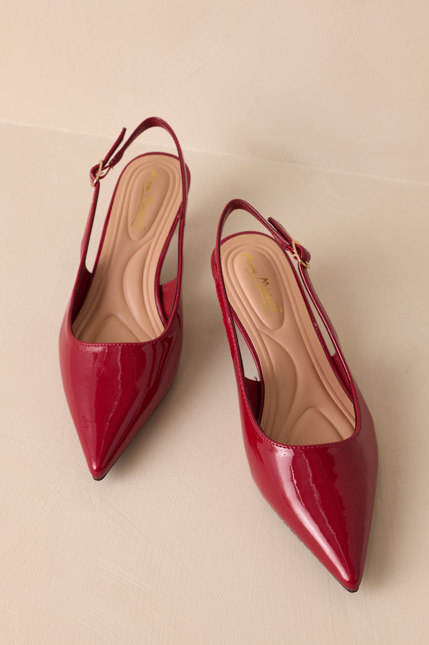 Overhead shot of a pair of burgundy heels displayed side by side, highlighting the pointed toe design, glossy patent material, adjustable slingback straps, and cushioned insoles for added comfort.