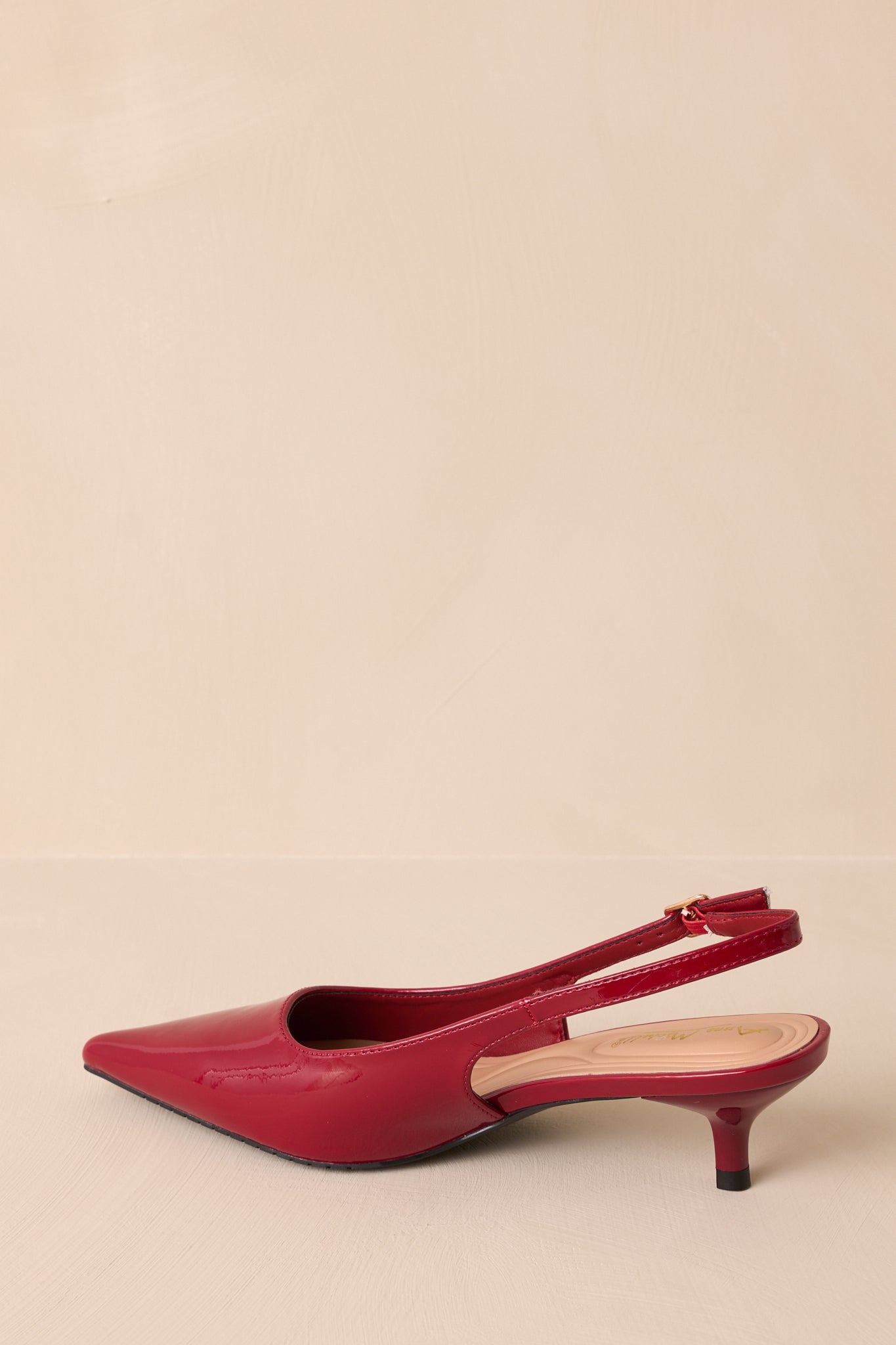 Side profile of a burgundy patent heel with a pointed toe, short kitten heel, and adjustable slingback strap. The cushioned insole is visible, offering added comfort to this elegant shoe.