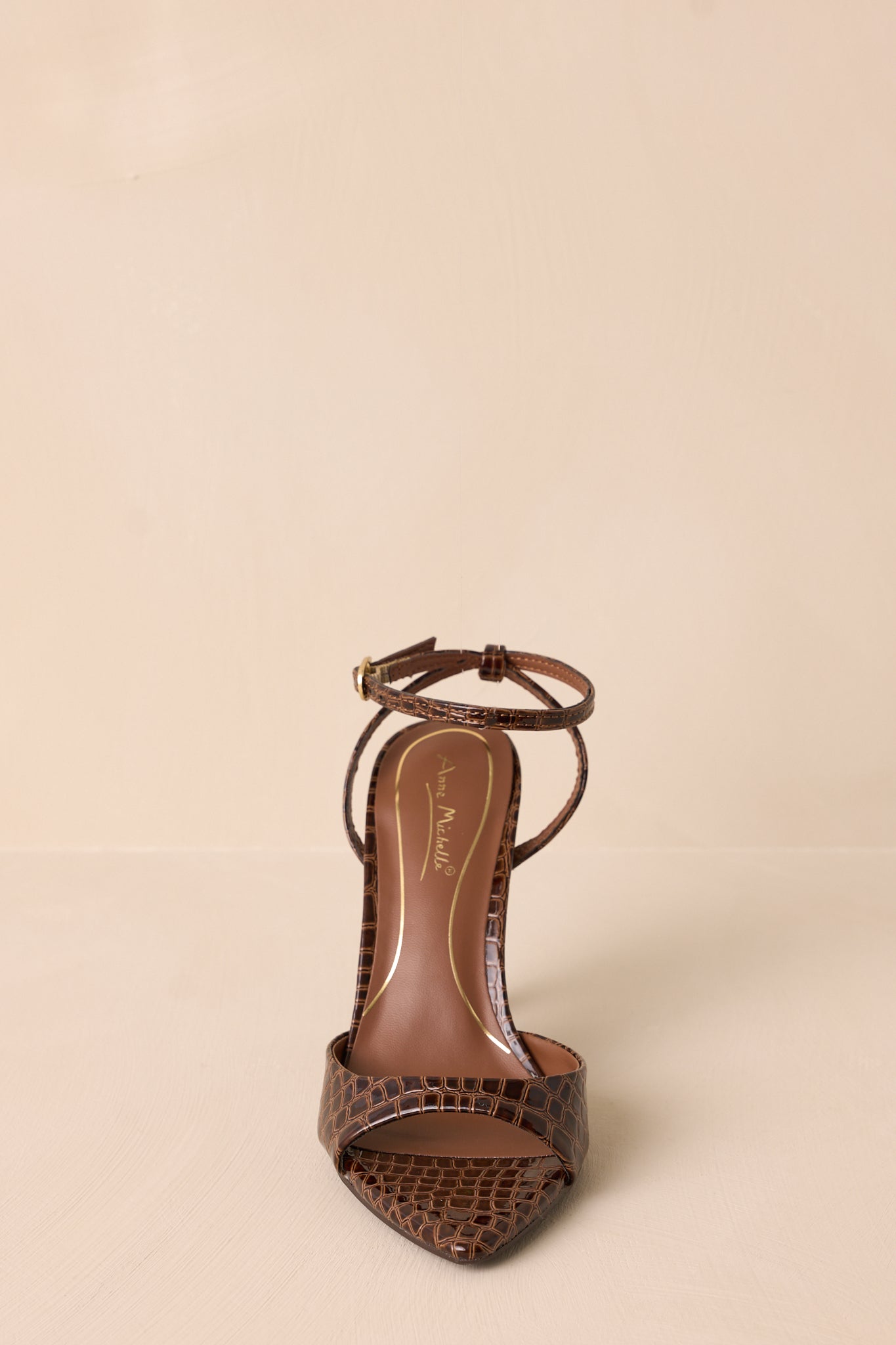 A front view of the brown heels, capturing the faux leather finish with the stiletto heel and wide toe strap in focus.