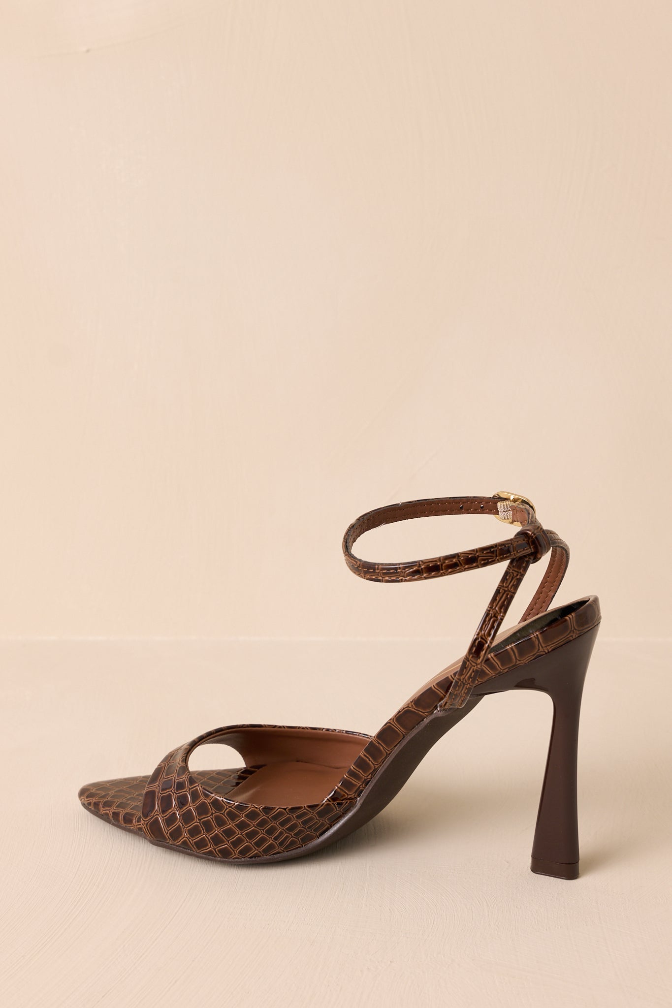 A side-close view of the brown heels, capturing the faux leather finish with the stiletto heel and wide toe strap in focus.