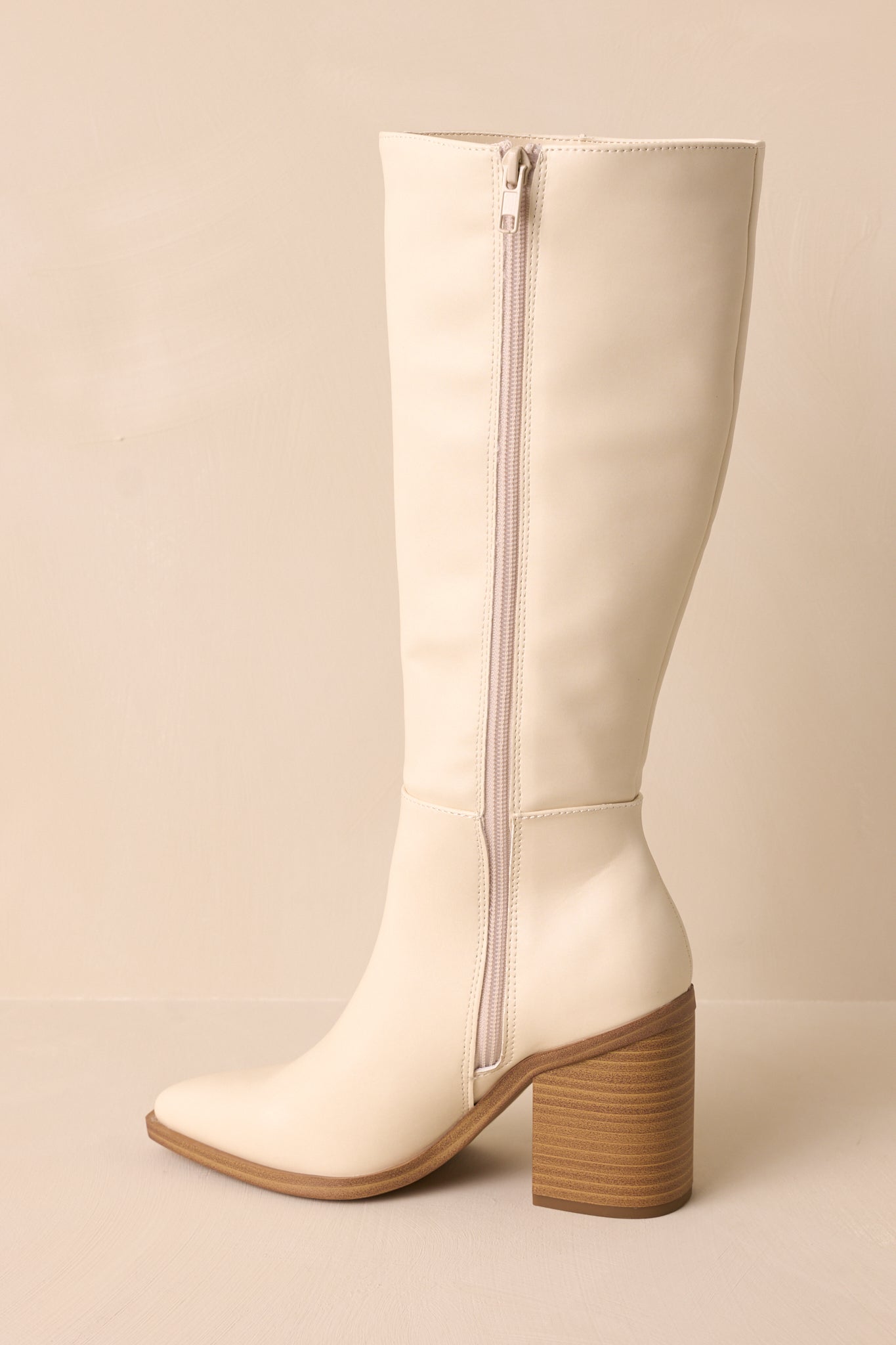 Side view showcasing the inside zipper on these knee high, faux leather ivory boots. 